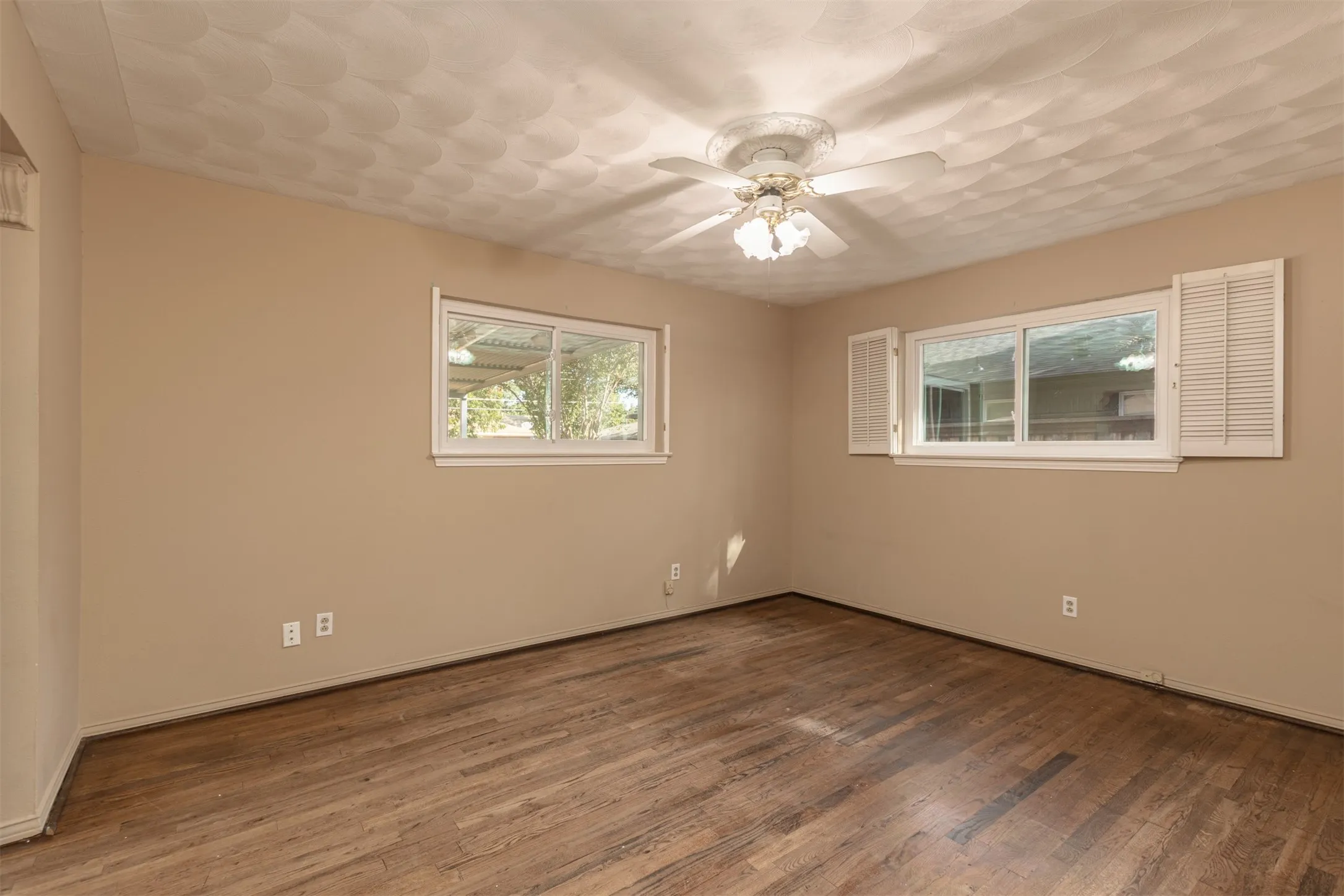 Wood-finish flooring, neutral wall tones, decorative ceiling fan, and multiple windows with white shutters