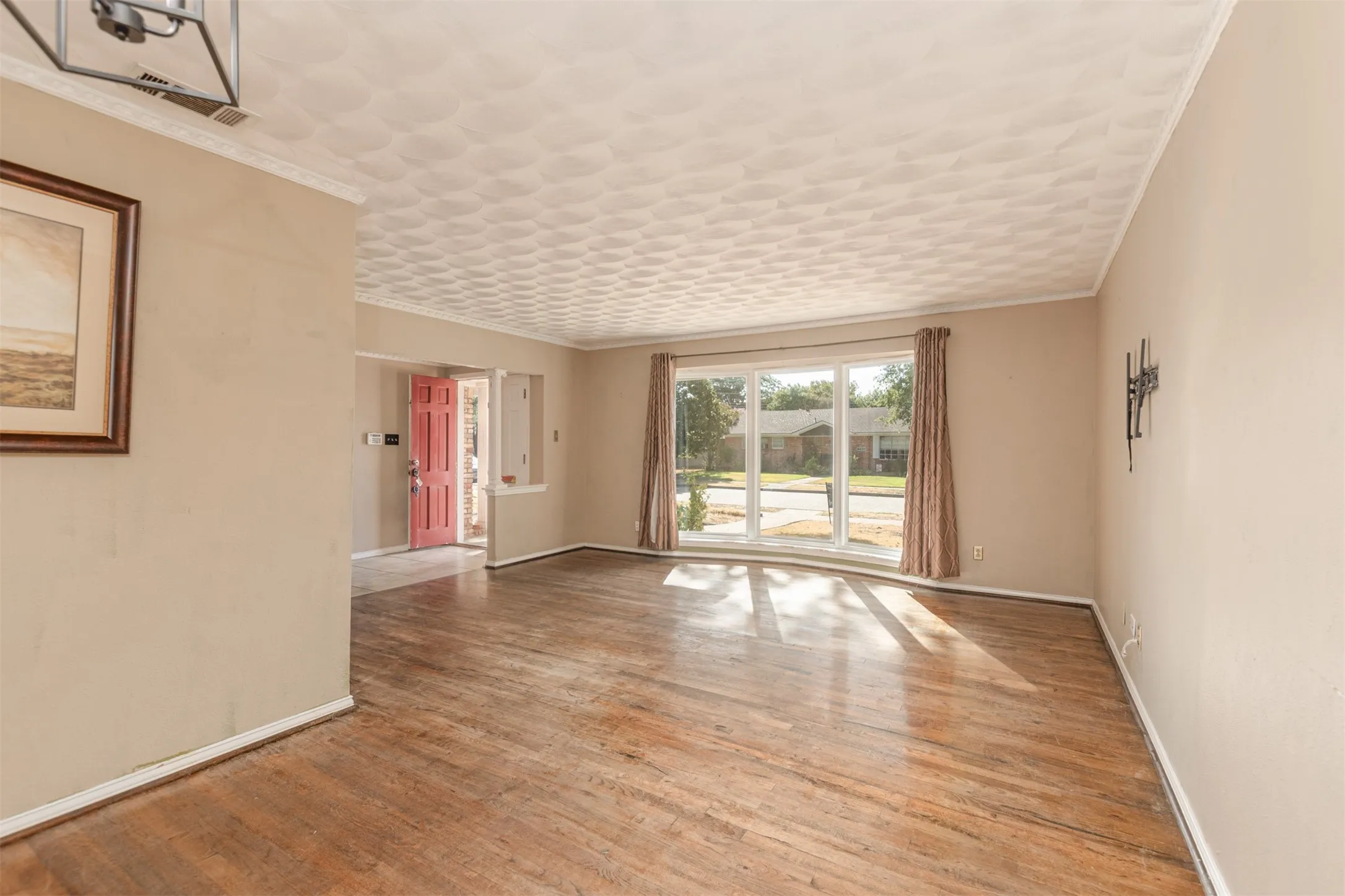 Hardwood flooring, expansive window, crown molding, neutral wall tones, and a bright interior door