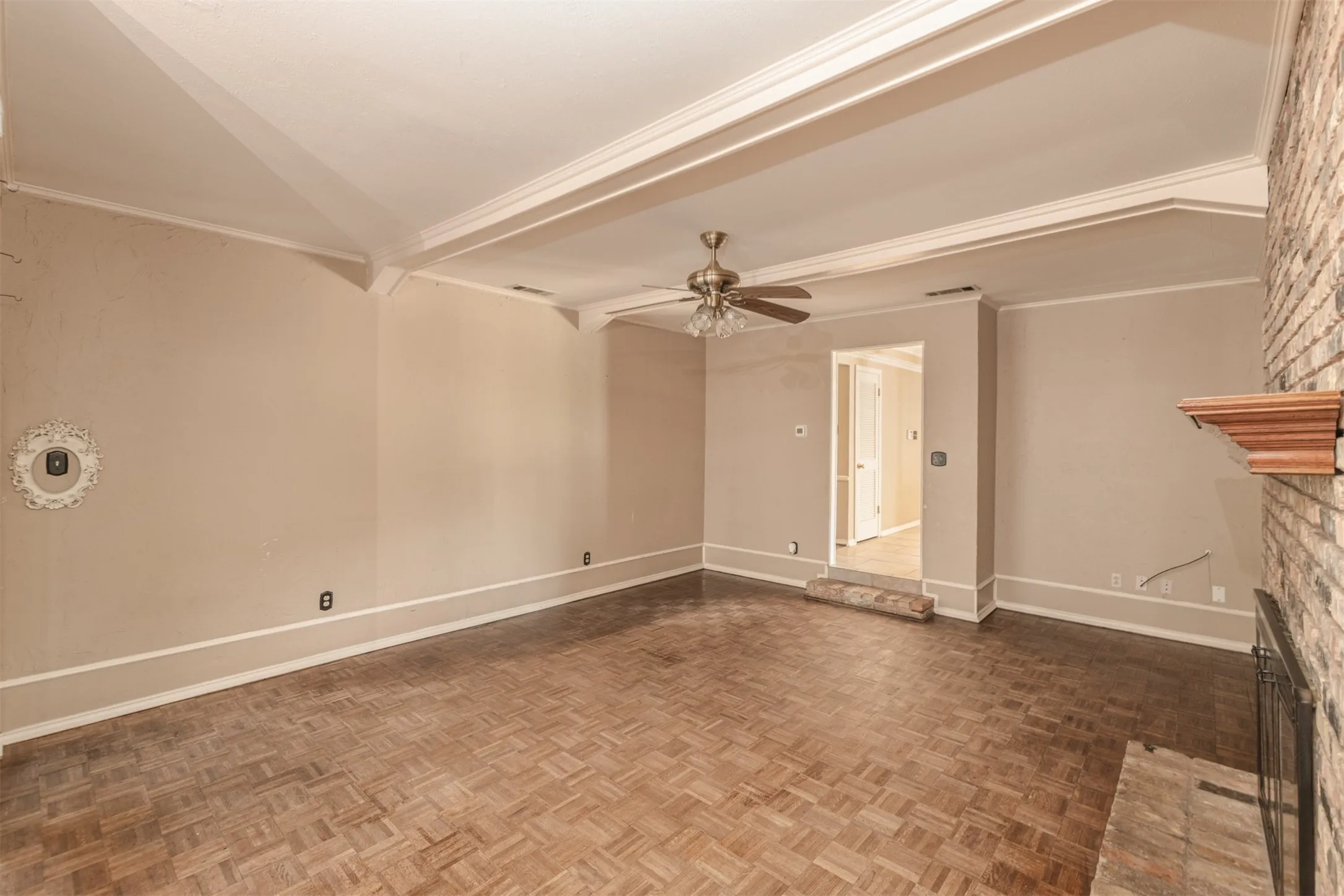Parquet wood-finish flooring, brick-clad fireplace with wood mantel, coffered ceiling, and ceiling fan with integrated lighting