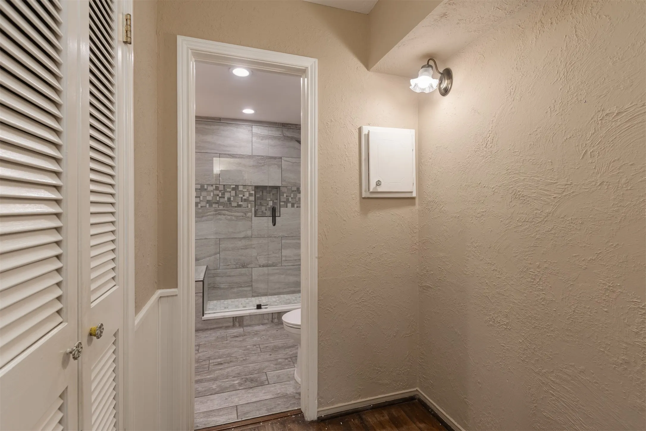 Louvered bifold doors with brass hardware, wainscoting, and wood-finish flooring