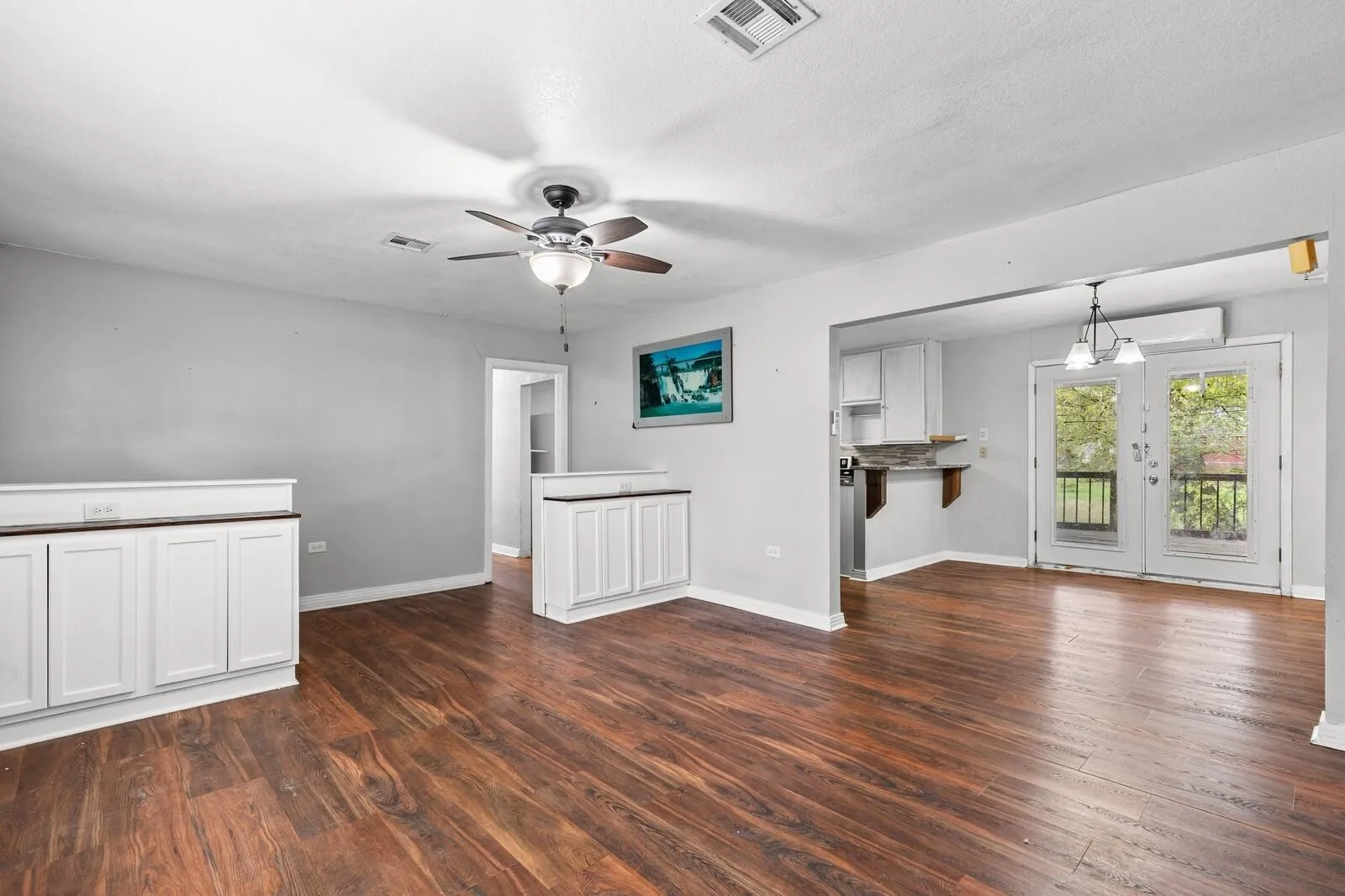 Wood-finish flooring throughout, white cabinetry with wood-tone countertops, ceiling fan, and double glass doors opening to the exterior