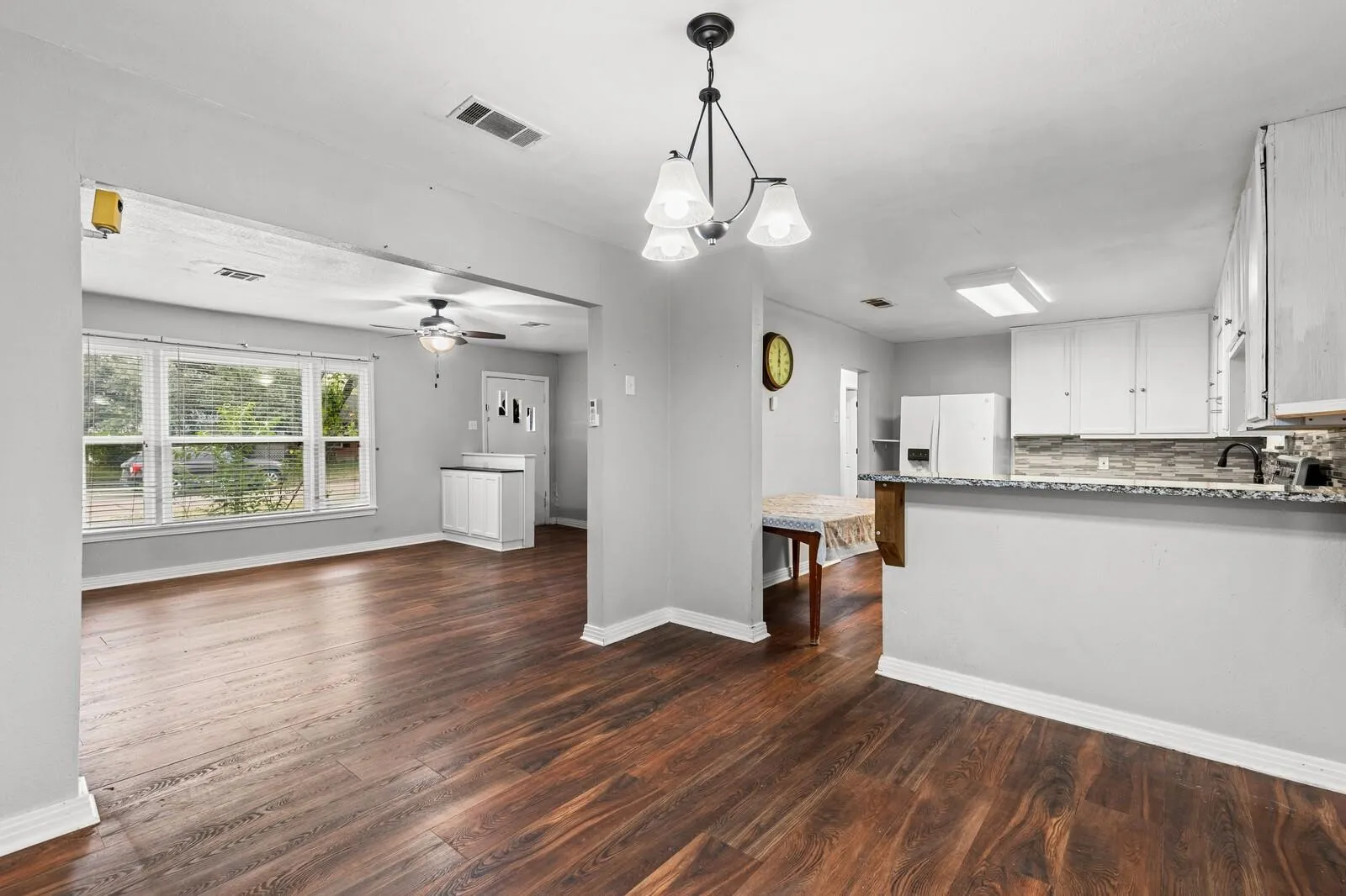 Wood-finish flooring throughout, white cabinetry, integrated kitchen appliances, and large windows with blinds