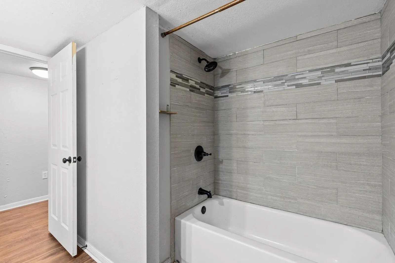 Bathtub with matte black fixtures, light gray horizontal tile surround, and a mosaic tile accent band