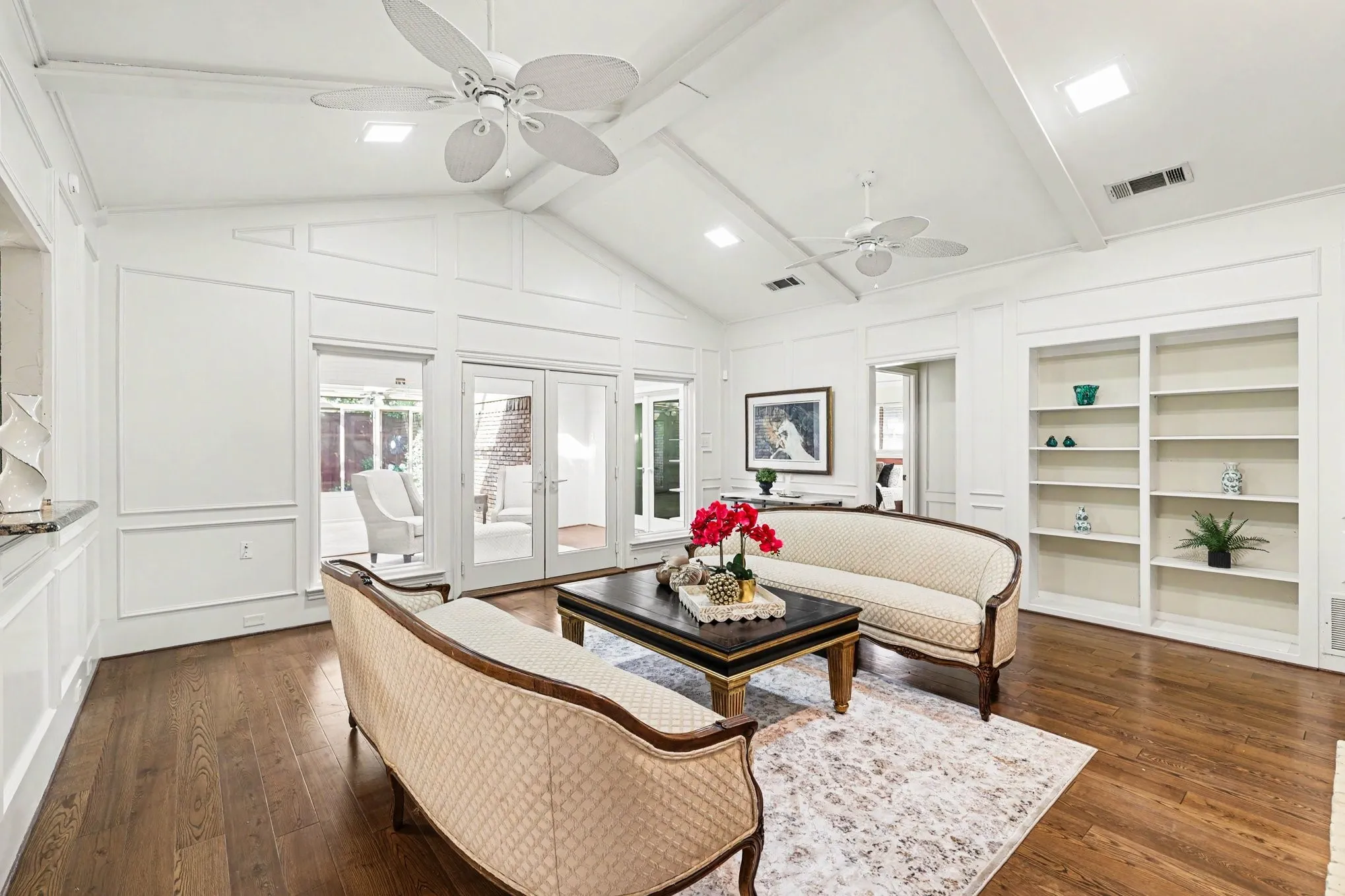 Vaulted ceiling with exposed beams, wood-finish flooring, built-in shelving, panel molding, and French doors