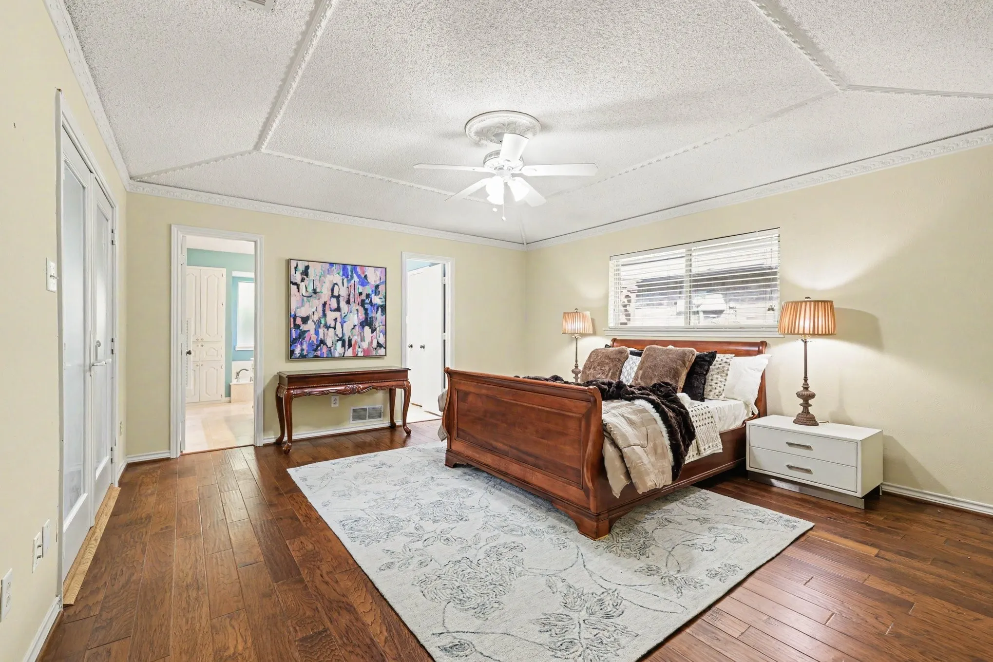 Hardwood-finish flooring, textured ceiling with decorative trim, white ceiling fan, and French doors