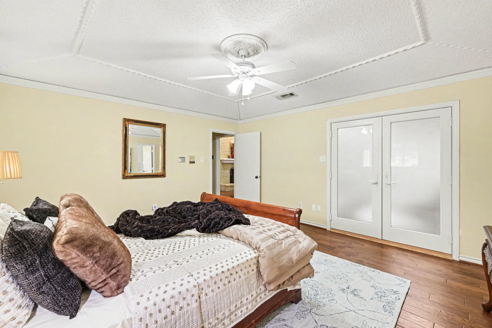 Wood-finish flooring, white double doors with frosted glass, ceiling fan with light fixture, decorative ceiling trim, and light yellow wall color