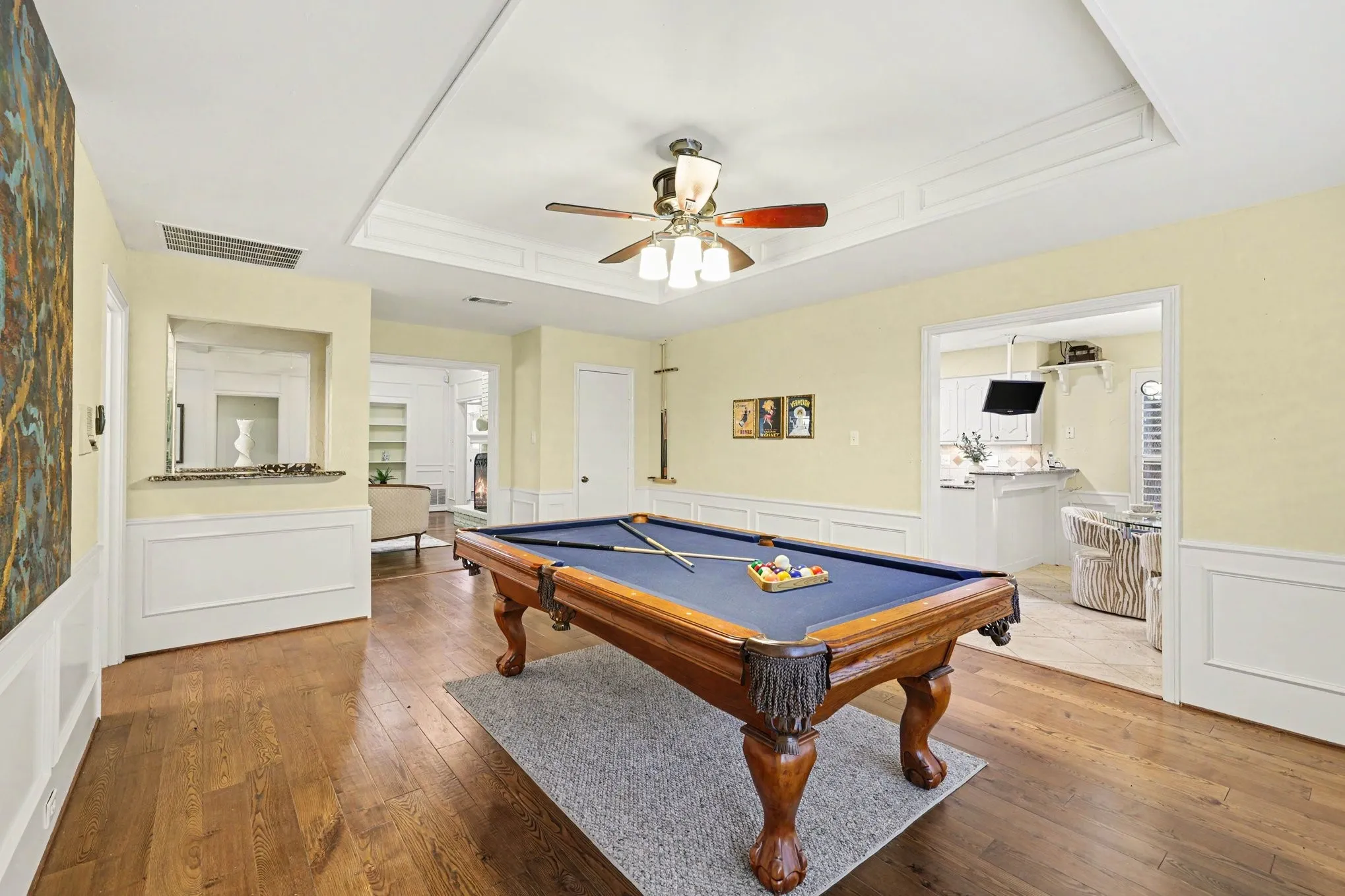 Wood-finish flooring throughout, tray ceiling with crown molding, ceiling fan with integrated lighting, and wainscoting on lower walls