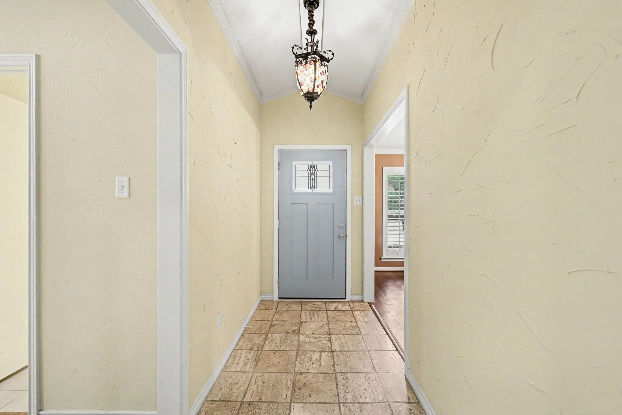 Vaulted ceiling with an ornamental chandelier, textured wall finish, and tile flooring