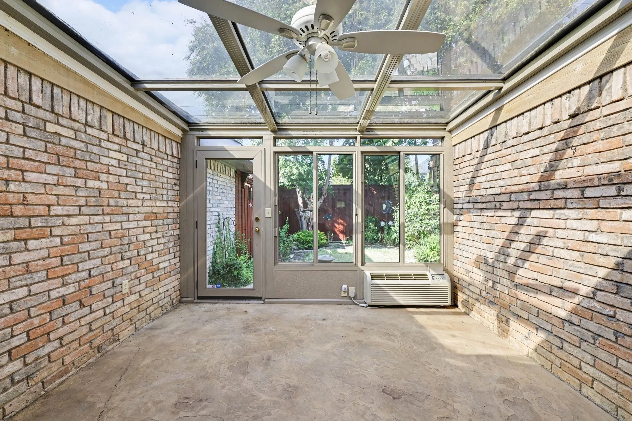 Sunroom with a glass roof, exposed brick walls, a ceiling fan, and concrete flooring