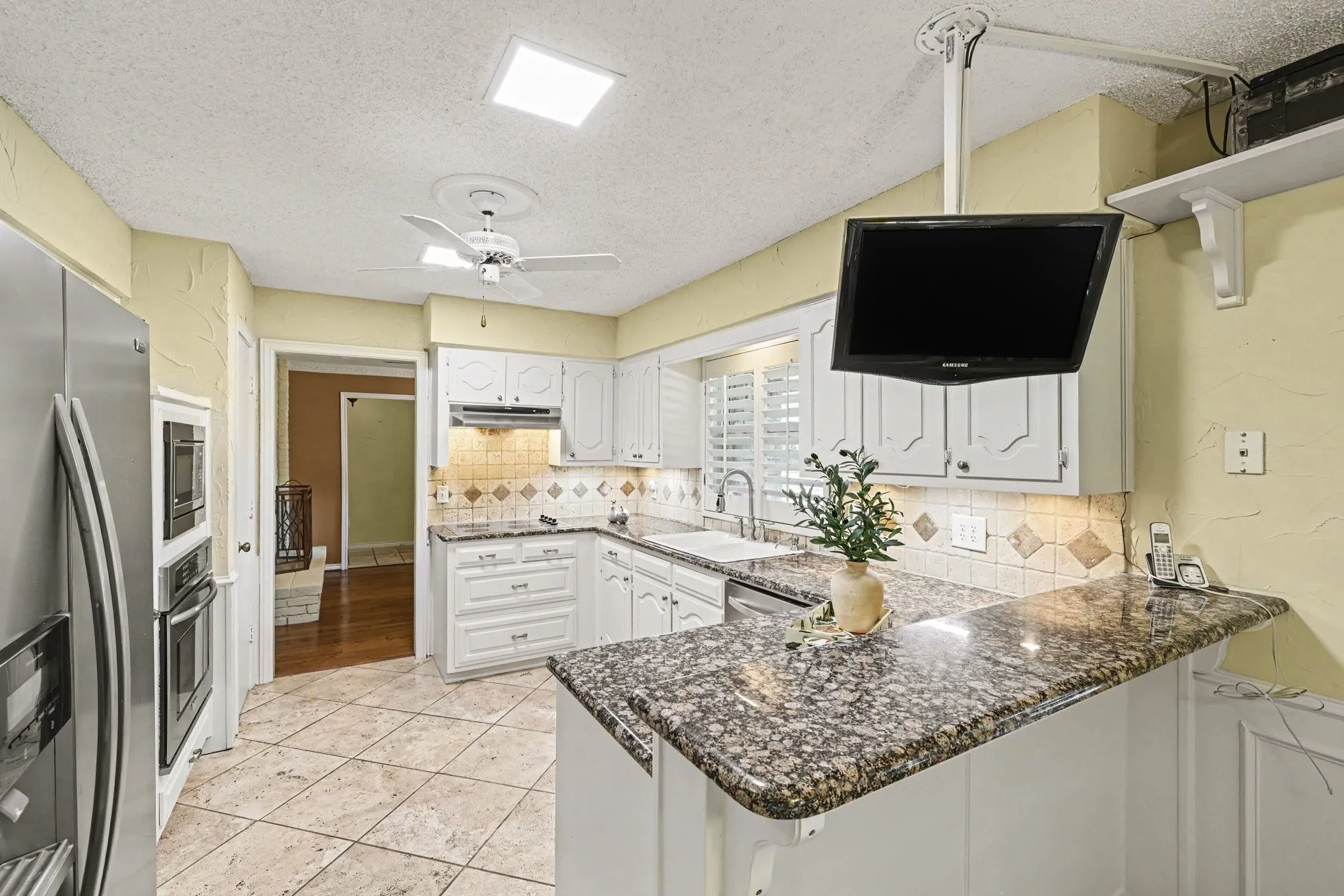 Kitchen featuring white cabinetry, granite countertops, tile backsplash, built-in stainless steel appliances, and a ceiling fan