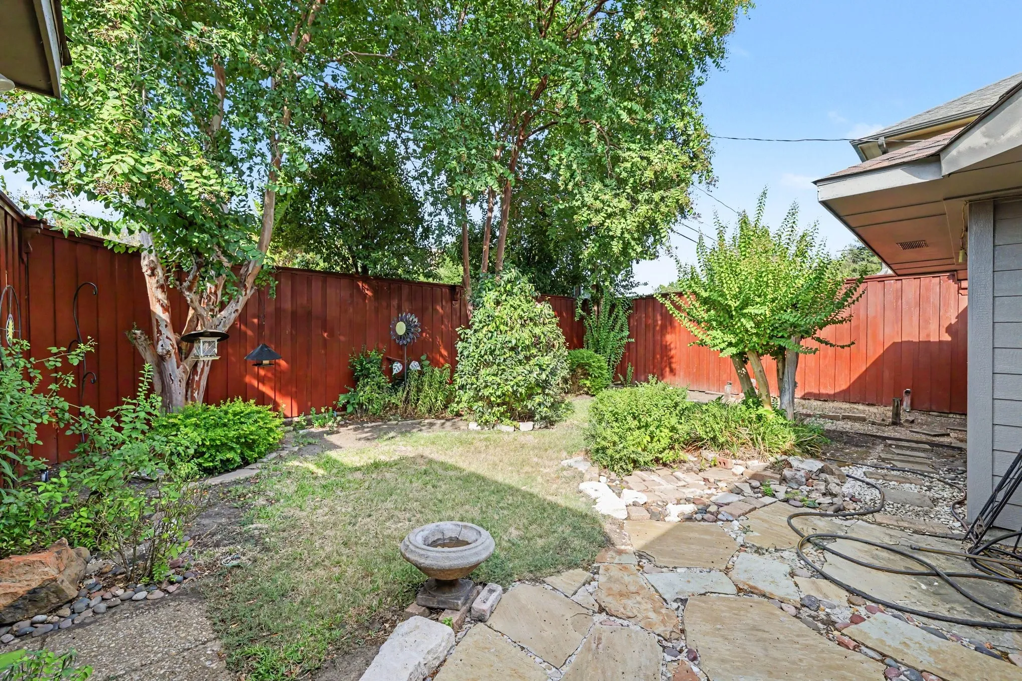 Fenced backyard featuring mature trees, established landscaping, and a flagstone patio