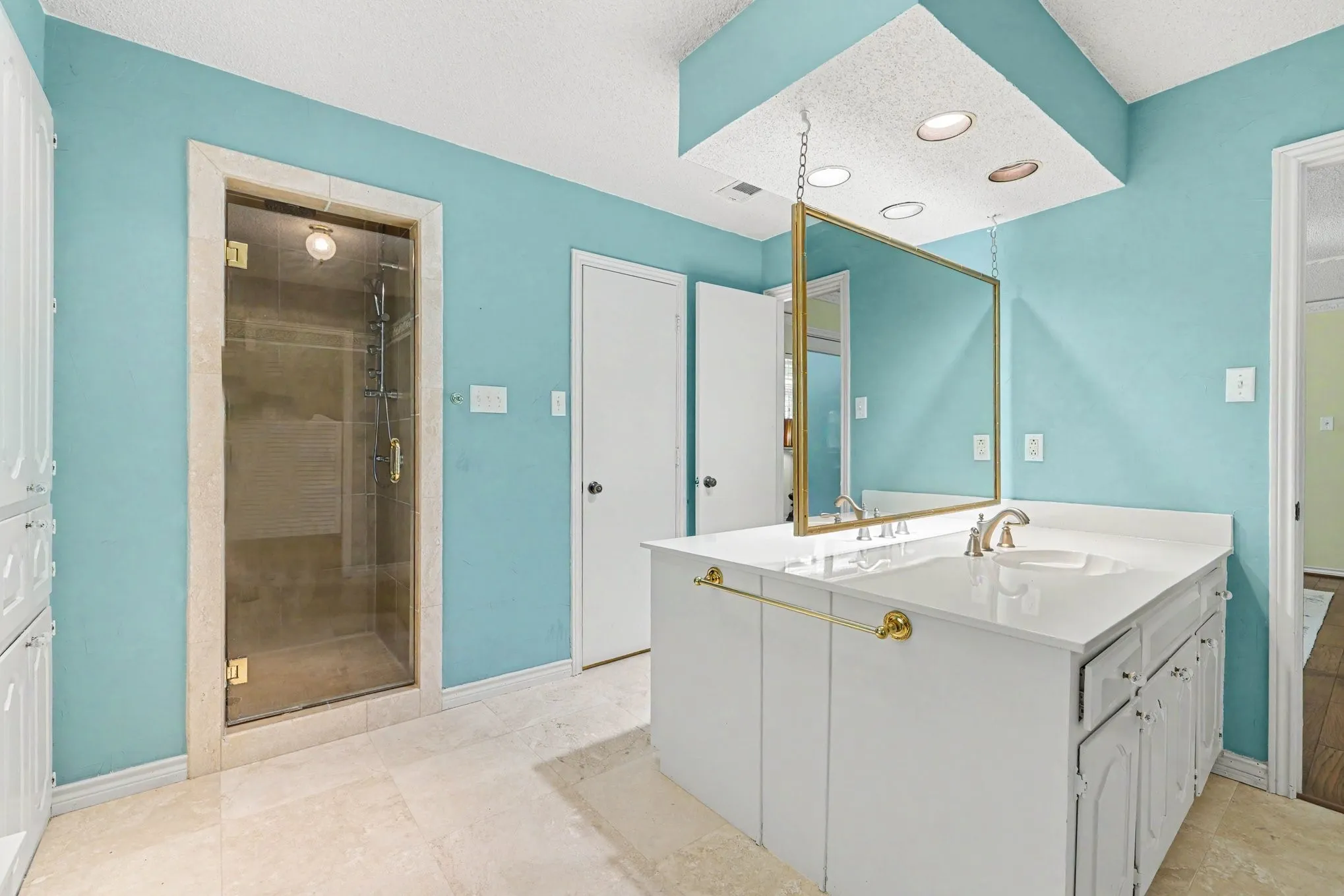 Glass-enclosed shower with a stone-look surround, dual vanity with white cabinetry, integrated sink, and suspended mirror