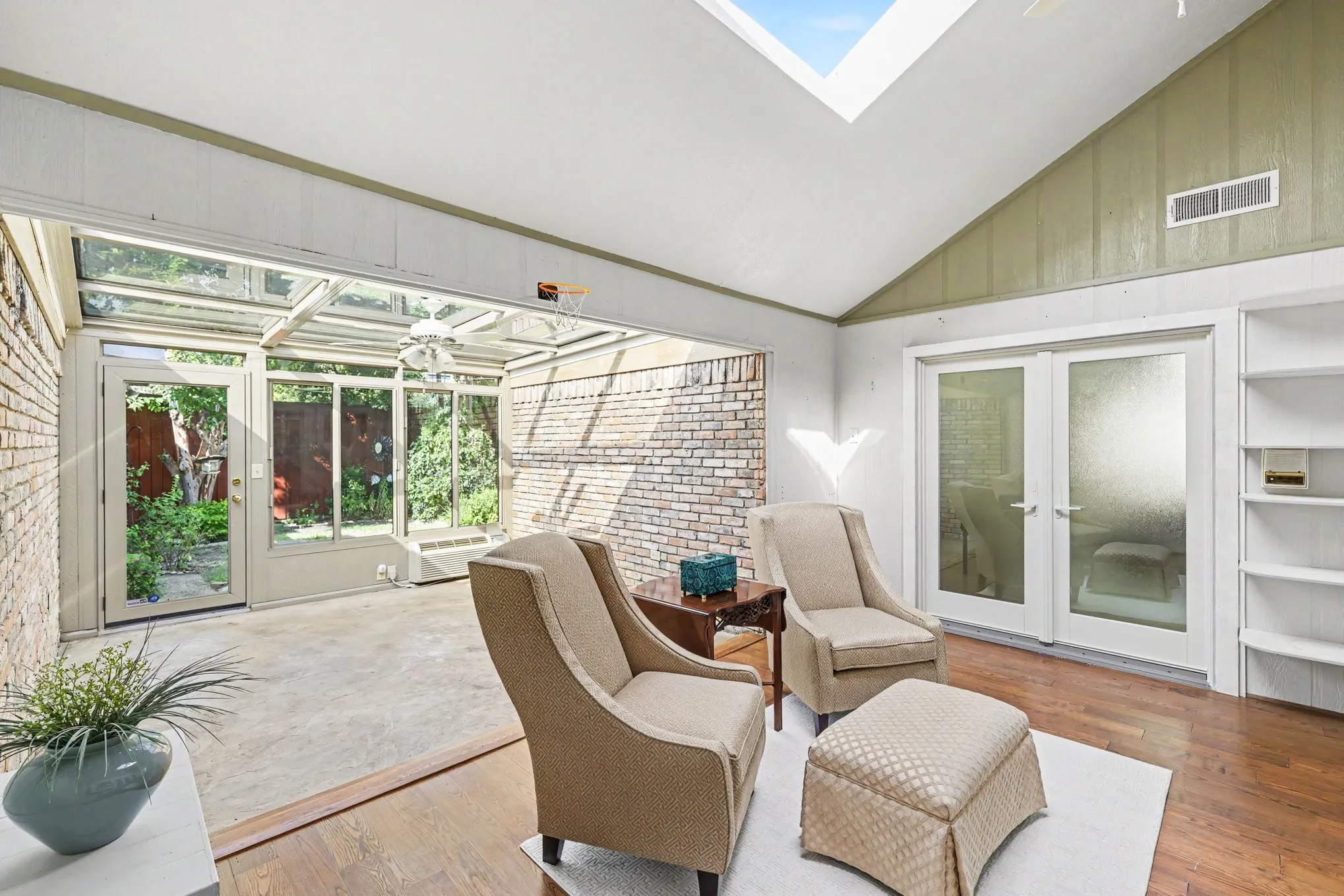 Vaulted ceiling with skylight, wood-finish flooring, built-in shelving, and frosted glass French doors