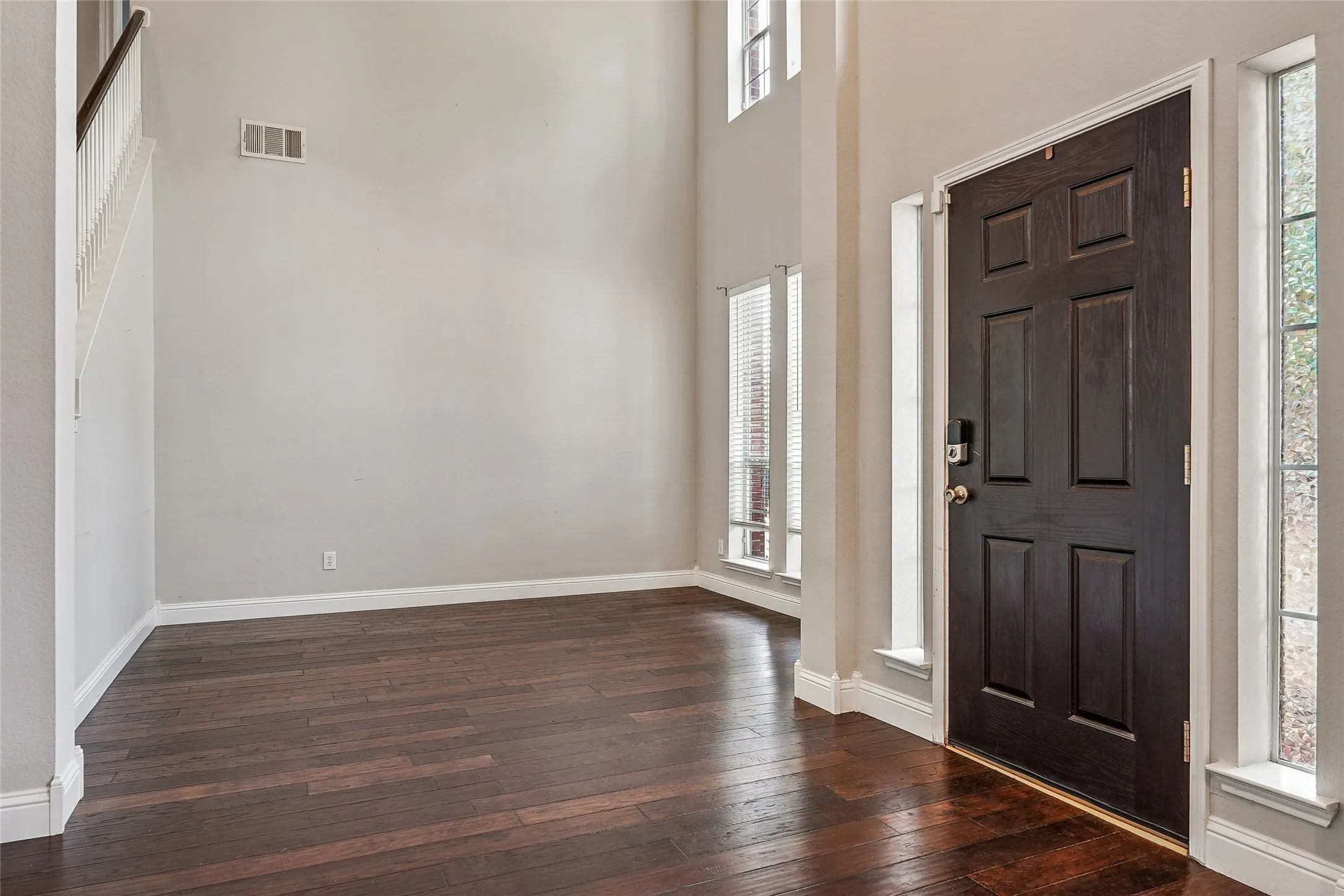 Foyer entrance with a high ceiling and dark wood-style floors. Area can be a living space or home office as illustrated.