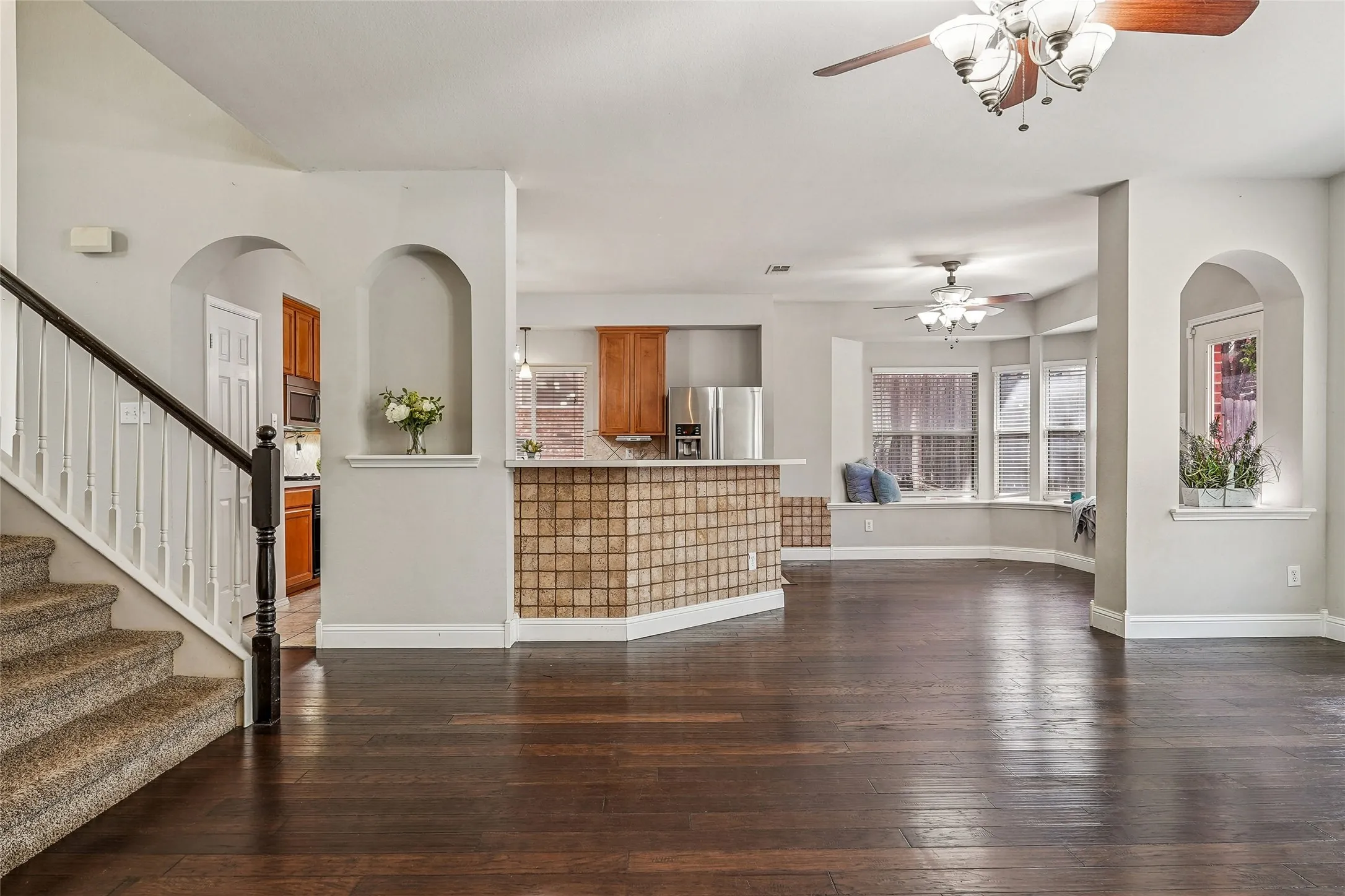 Unfurnished living room with arched walkways, dark wood-type flooring, and a ceiling fan
