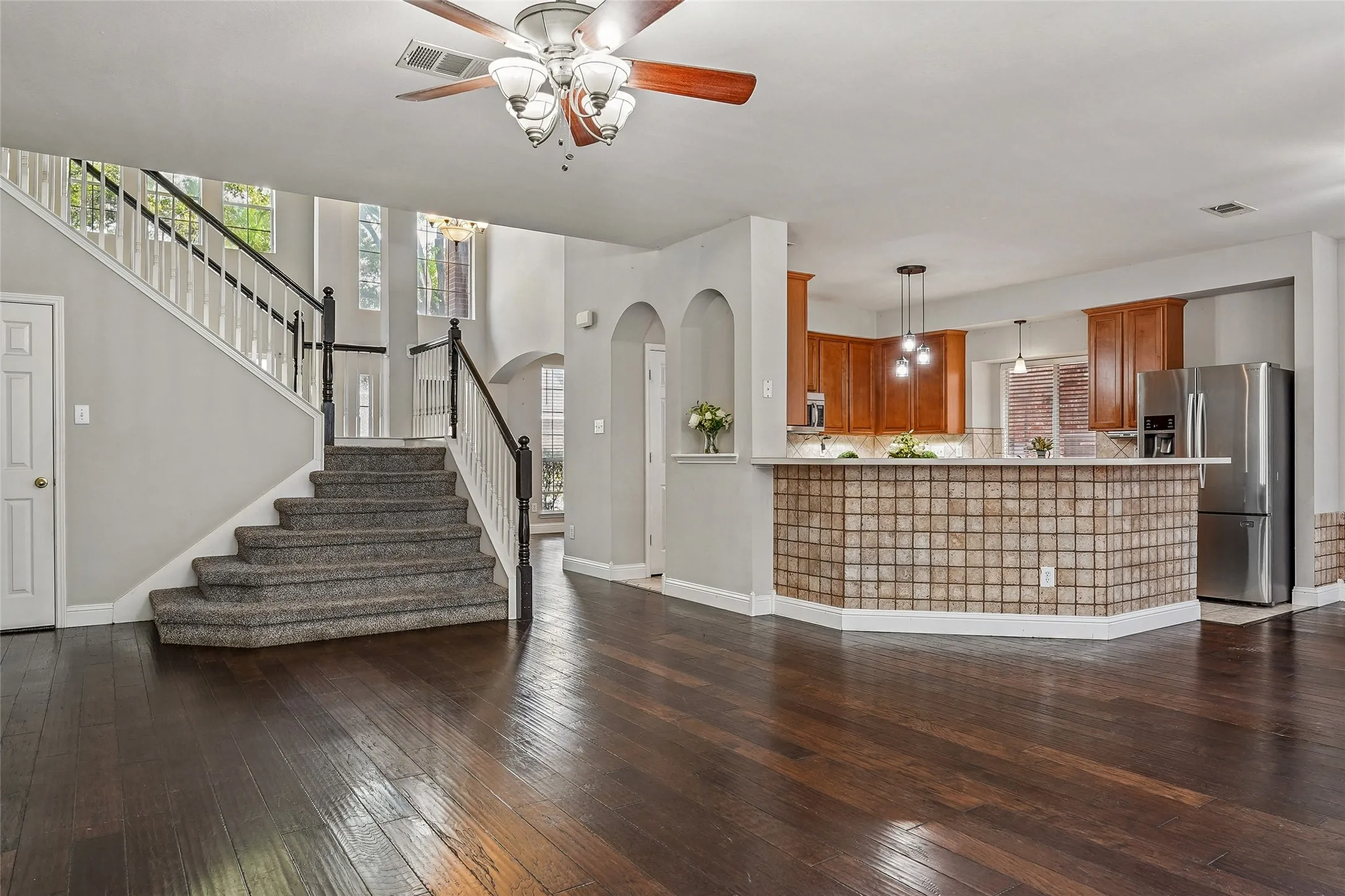 Unfurnished living room featuring arched walkways, dark wood finished floors, and a ceiling fan