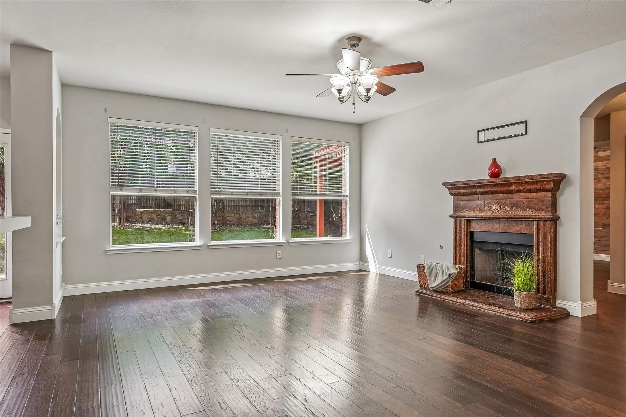 Unfurnished living room with ceiling fan, a fireplace with raised hearth, dark wood-style floors, and arched walkways