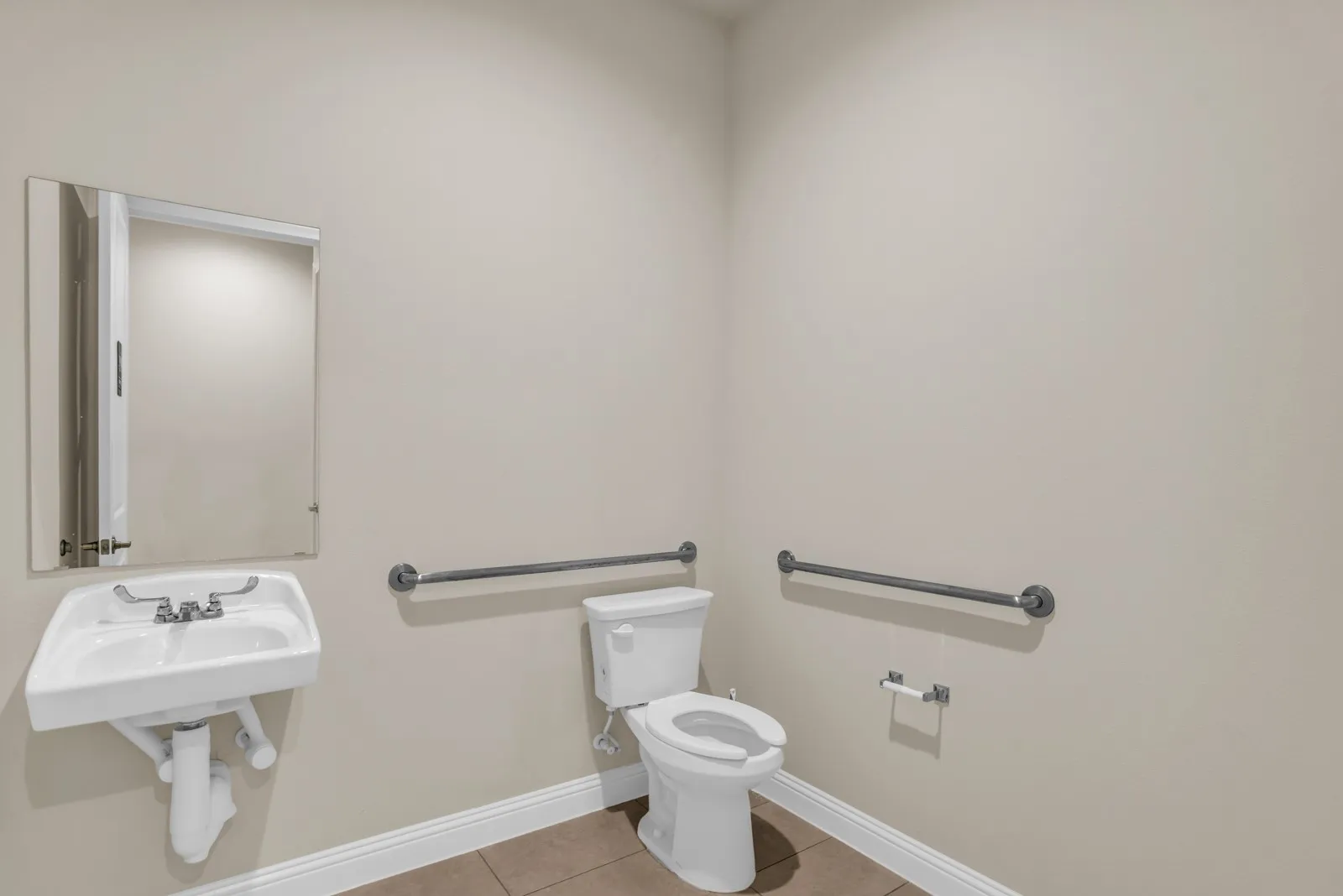 Wall-mounted sink with mirror, toilet, and dual grab bars on neutral-toned walls