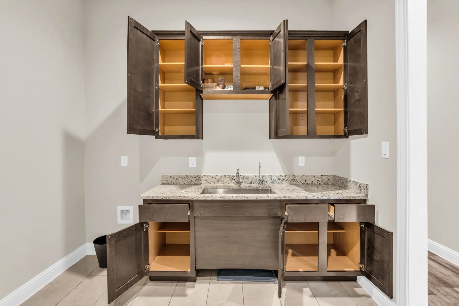 Wet bar featuring dark wood-finish cabinetry, a speckled countertop, an undermount sink, and wood-finish flooring