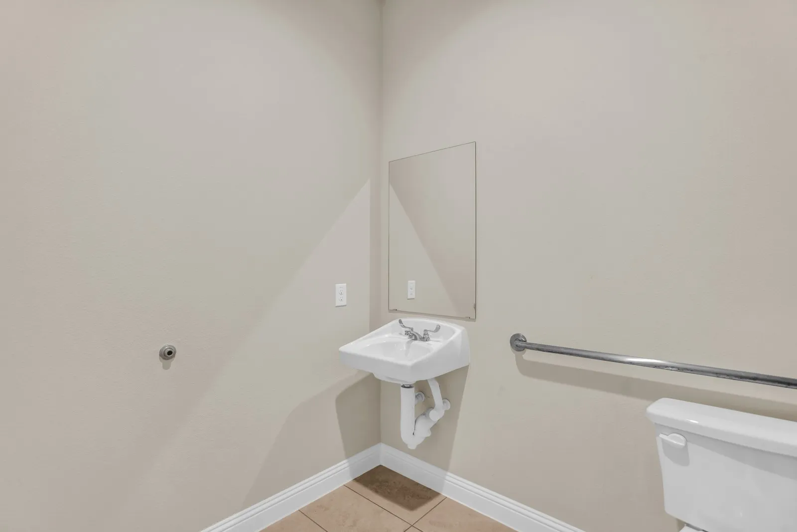 Wall-mounted sink with mirror, toilet, and a grab bar, set on tiled flooring