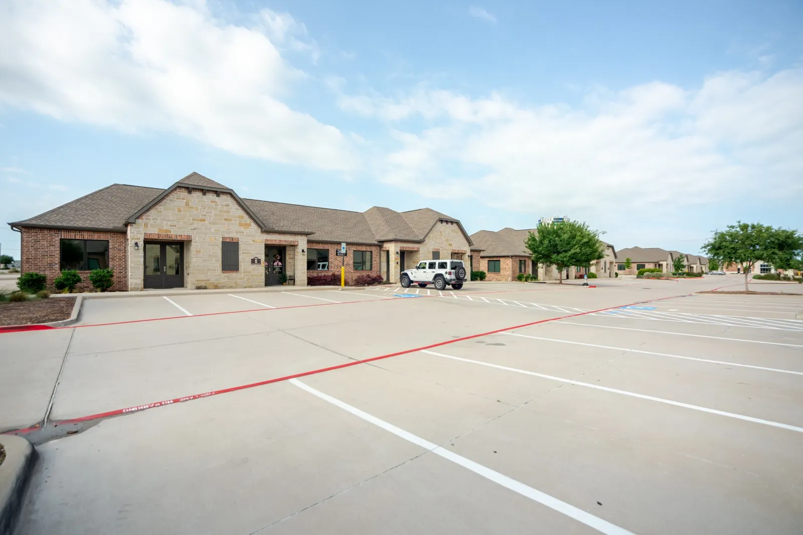 Stone and brick facade with multiple gabled roofs, a prominent central entrance, and a large paved parking area