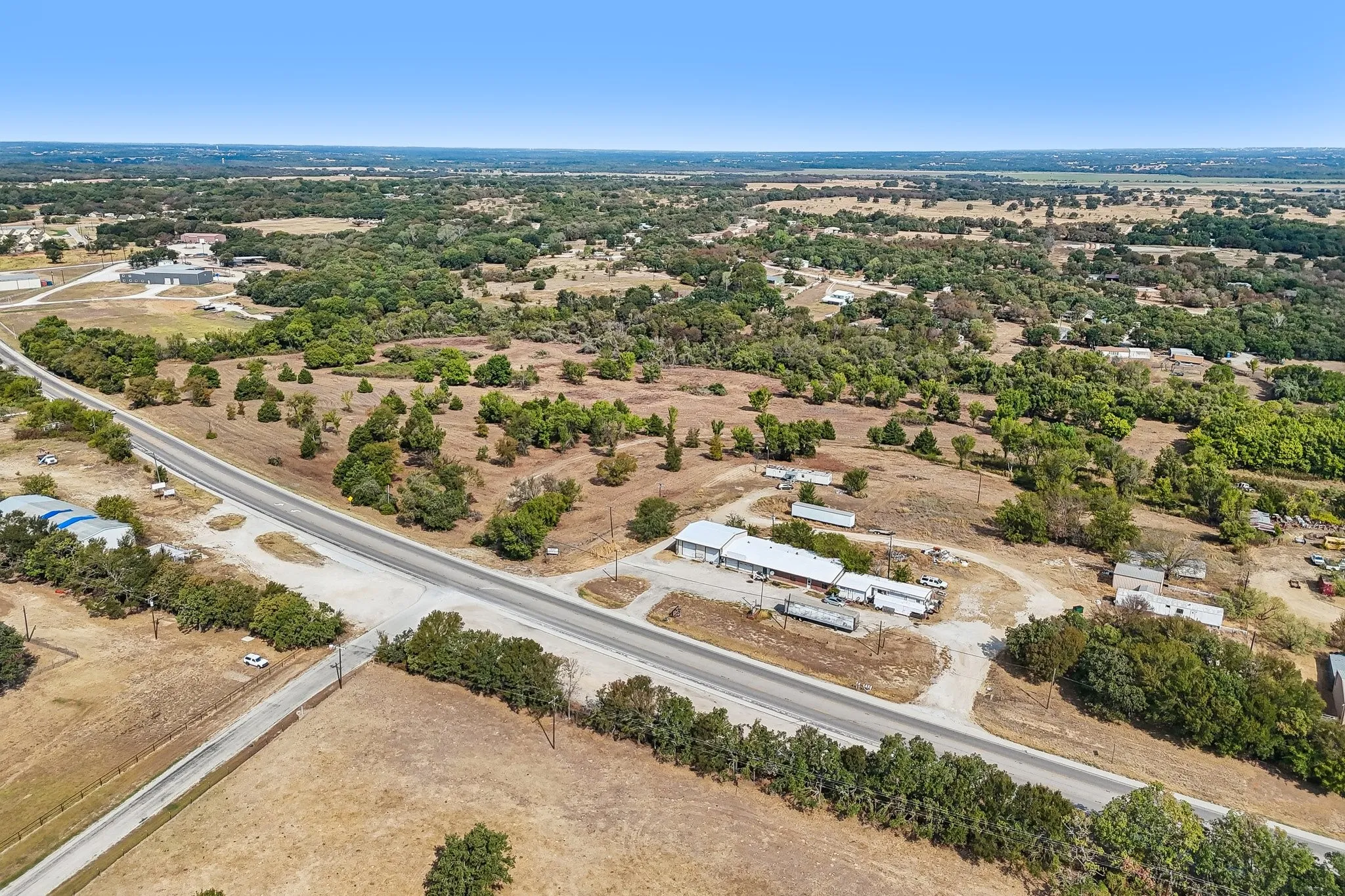 Expansive undeveloped land featuring a paved roadway and scattered mature trees