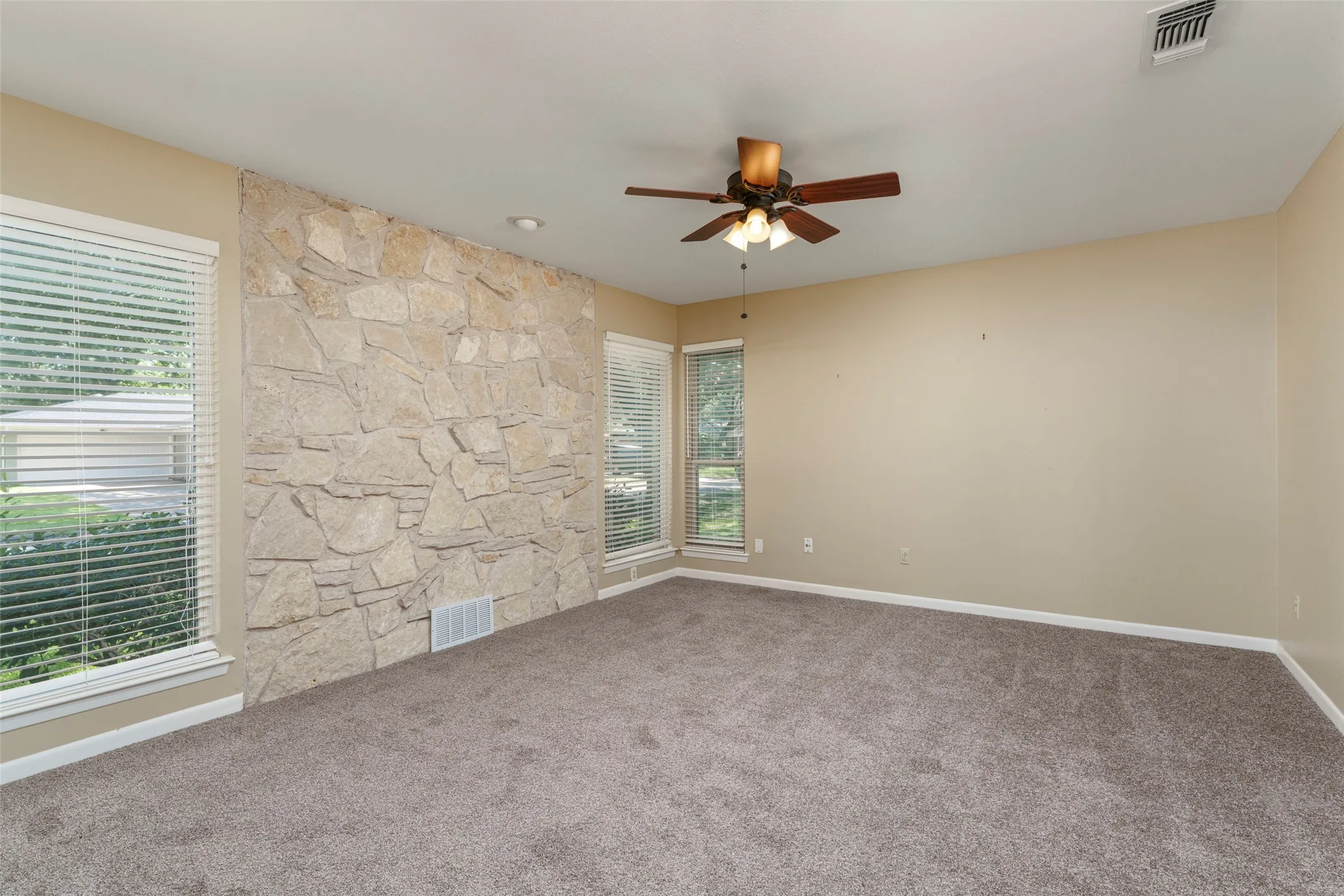 Stone accent wall with a wood-finish ceiling fan and recessed lighting