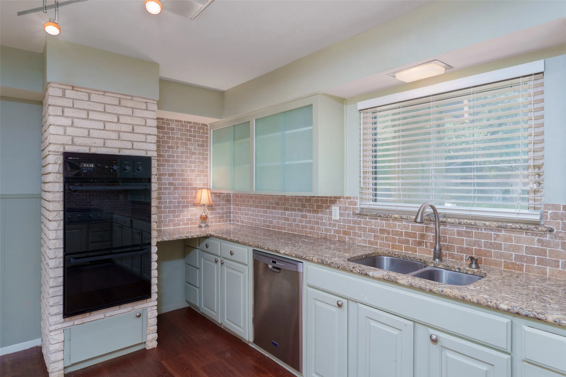 Built-in double oven, dual basin sink, stainless steel dishwasher, wood-finish flooring, and track lighting