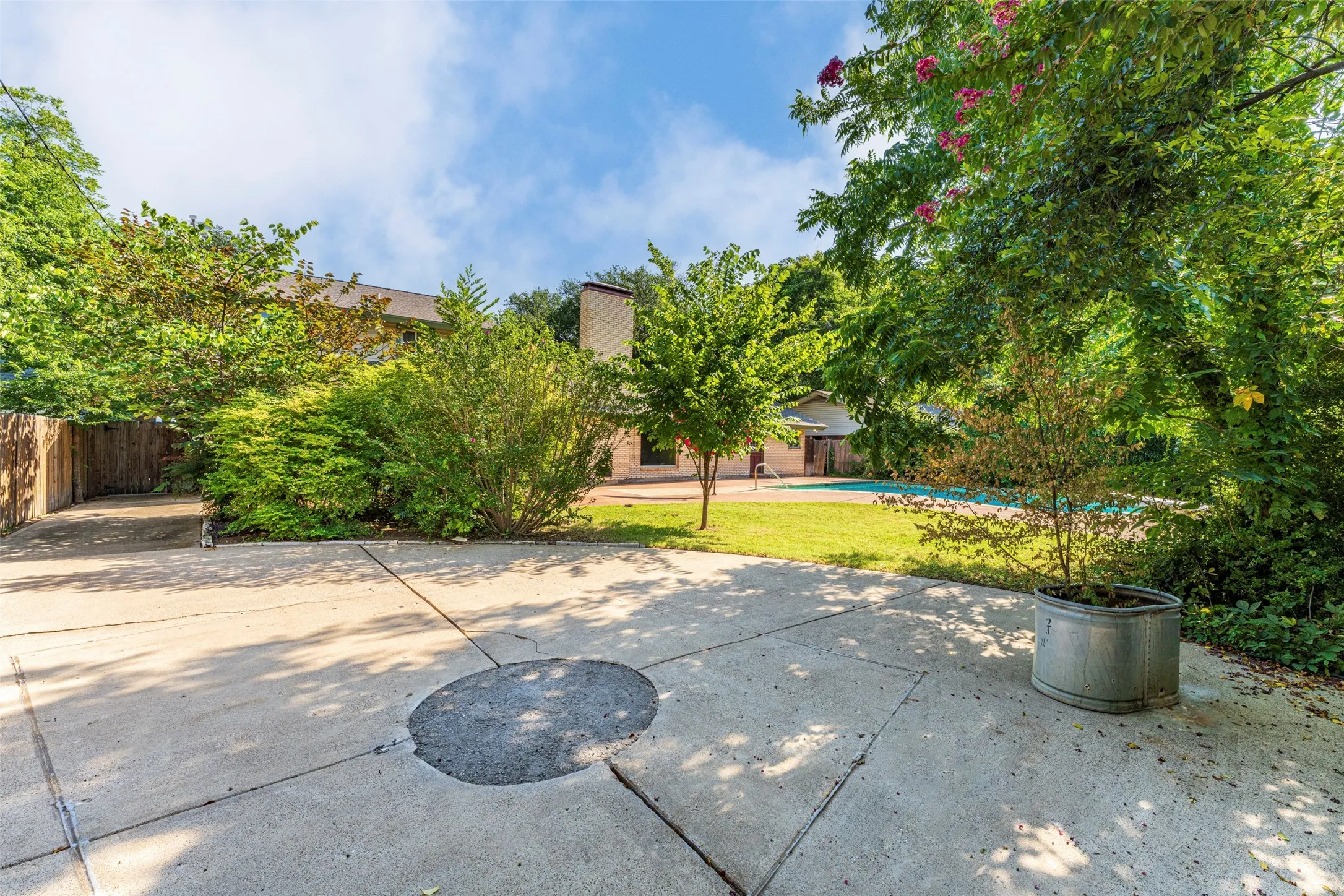 Expansive concrete patio area with mature trees and lush landscaping