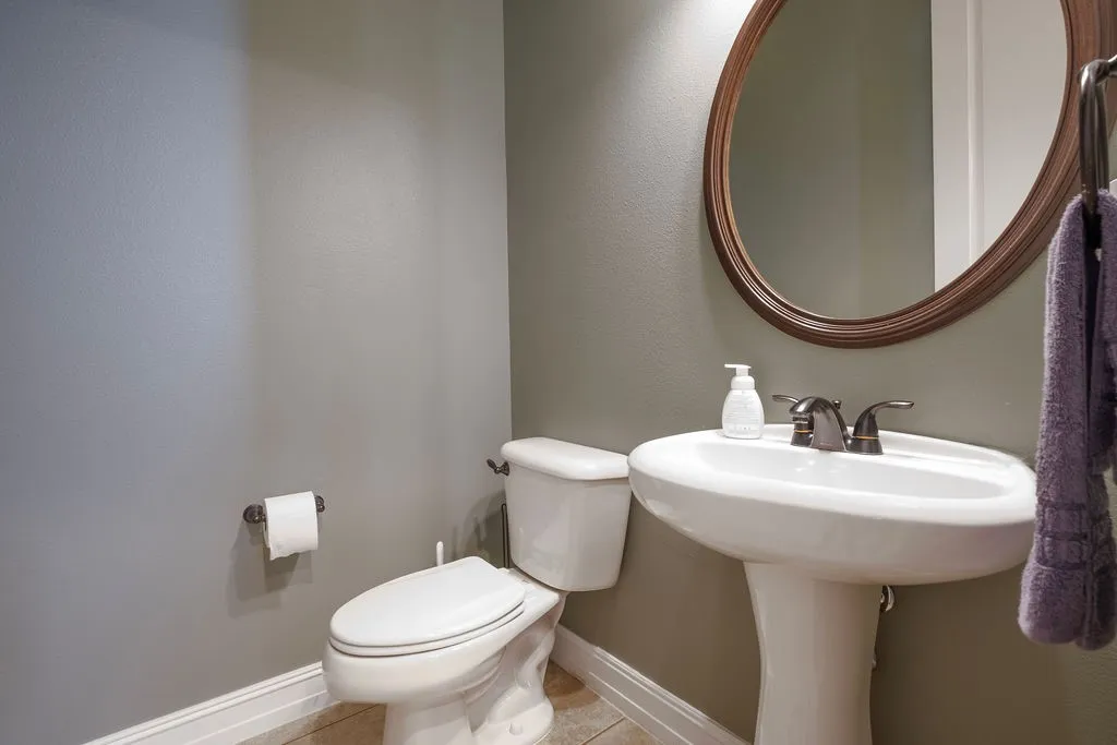 Pedestal sink with bronze-finish faucet, elongated toilet, and wall-mounted oval mirror