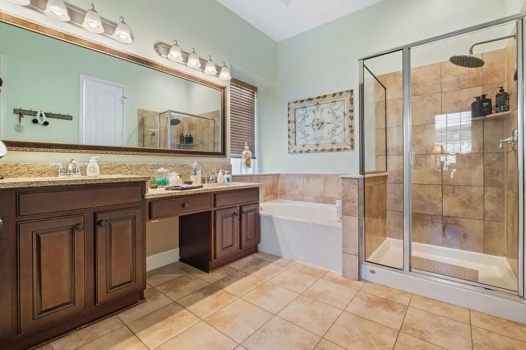 Dual vanity with stone-finish countertop, wood-finish cabinetry, and an expansive mirror