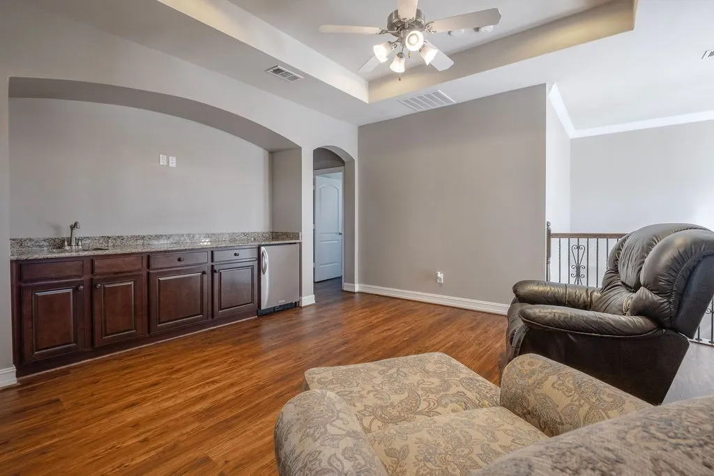 Wood-finish flooring, built-in cabinetry with a countertop and sink, tray ceiling, ceiling fan, and an open railing