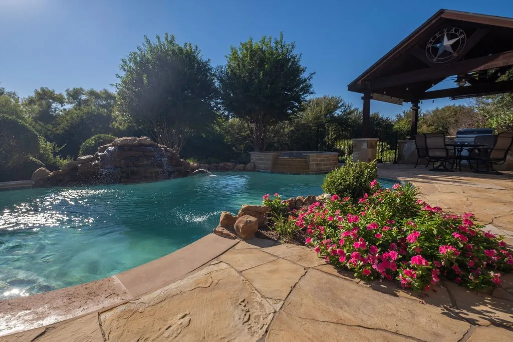 Swimming pool with rock waterfall feature, flagstone patio, covered outdoor living area with wood beams, and integrated hot tub