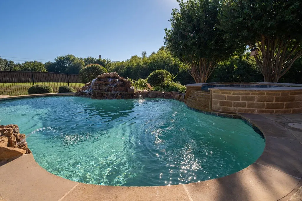 Sparkling swimming pool with a rock waterfall feature, integrated spa, and surrounding stone coping
