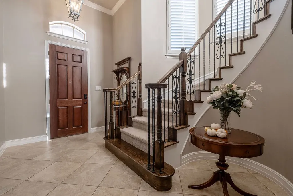 Wood panel front door with arched transom window, tiled flooring, grand staircase with wrought iron balusters, wood handrail, and carpeted treads