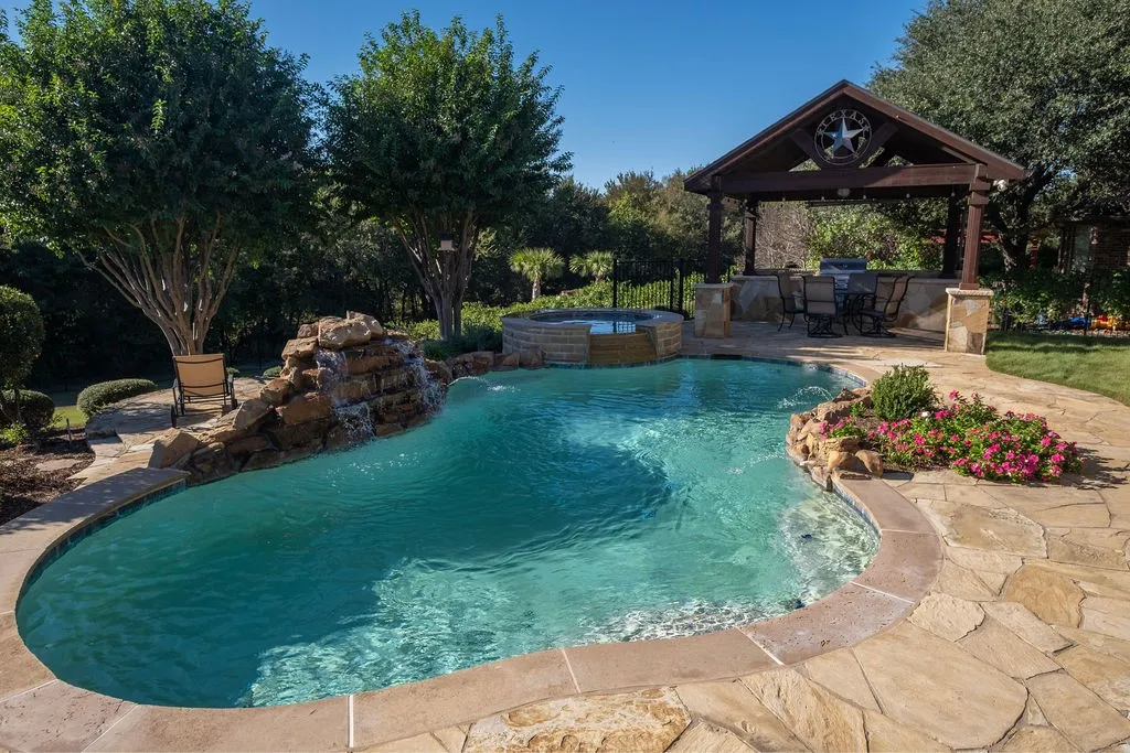Freeform swimming pool with a rock waterfall, integrated spa, and flagstone coping