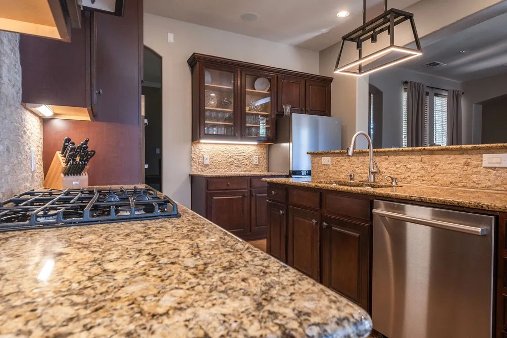 Granite countertops, dark wood-finish cabinetry, stainless steel appliances, gas cooktop, and an undermount sink with a gooseneck faucet