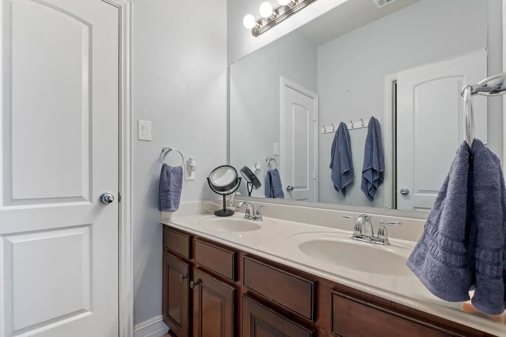Dual undermount sinks with chrome faucets, set in a light-toned countertop, above a dark wood-finish vanity