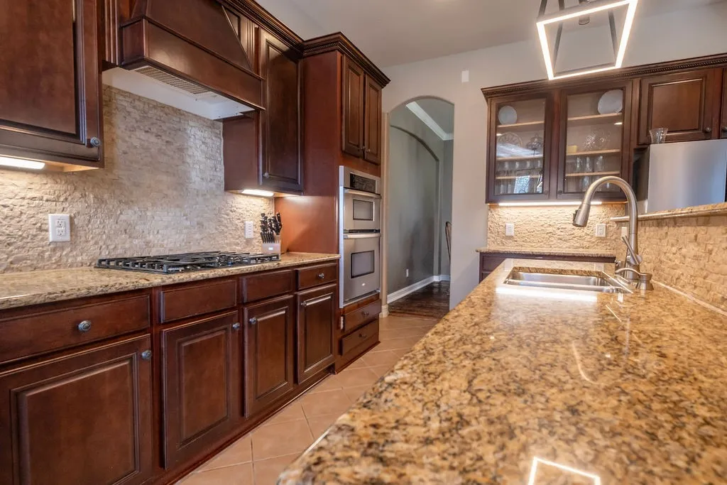 Rich wood cabinetry, stainless steel appliances, stone tile backsplash, and granite countertops