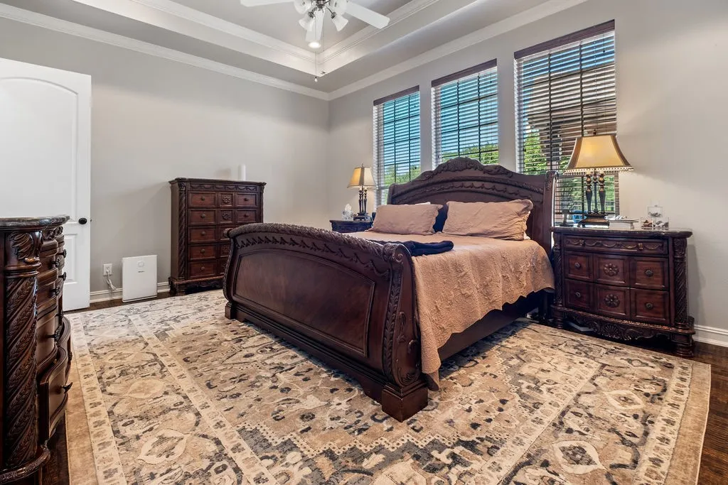 Tray ceiling with crown molding, ceiling fan, wood-finish flooring, white paneled interior door, and multiple windows