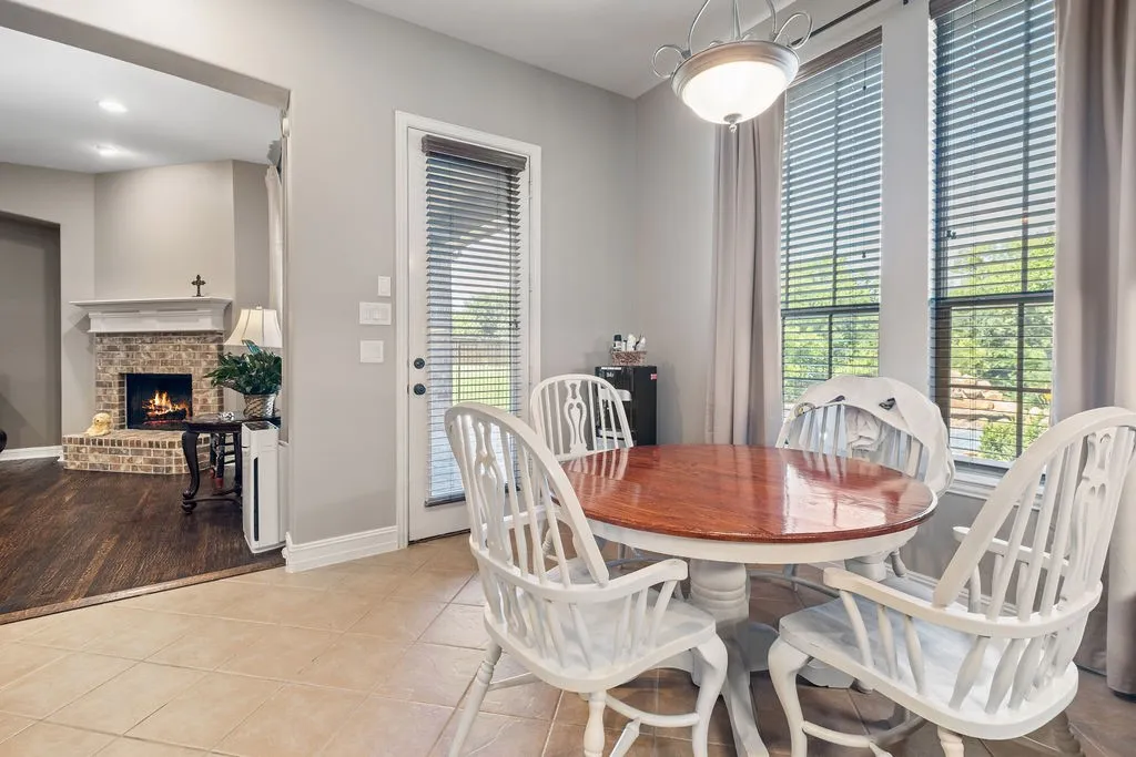 Tile flooring, full-light door, dual windows with blinds and drapery, overhead lighting fixture, and a partial brick fireplace with mantel