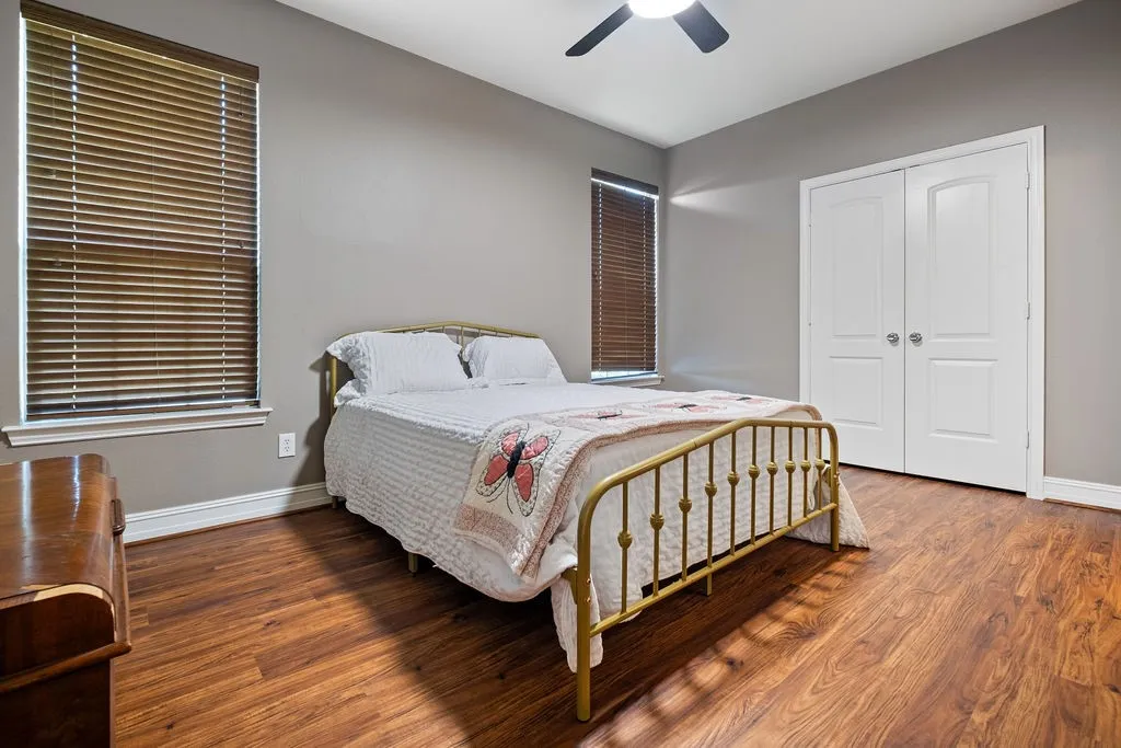 Wood-finish flooring, dual windows with blinds, bi-fold closet doors, and a ceiling fan with integrated lighting