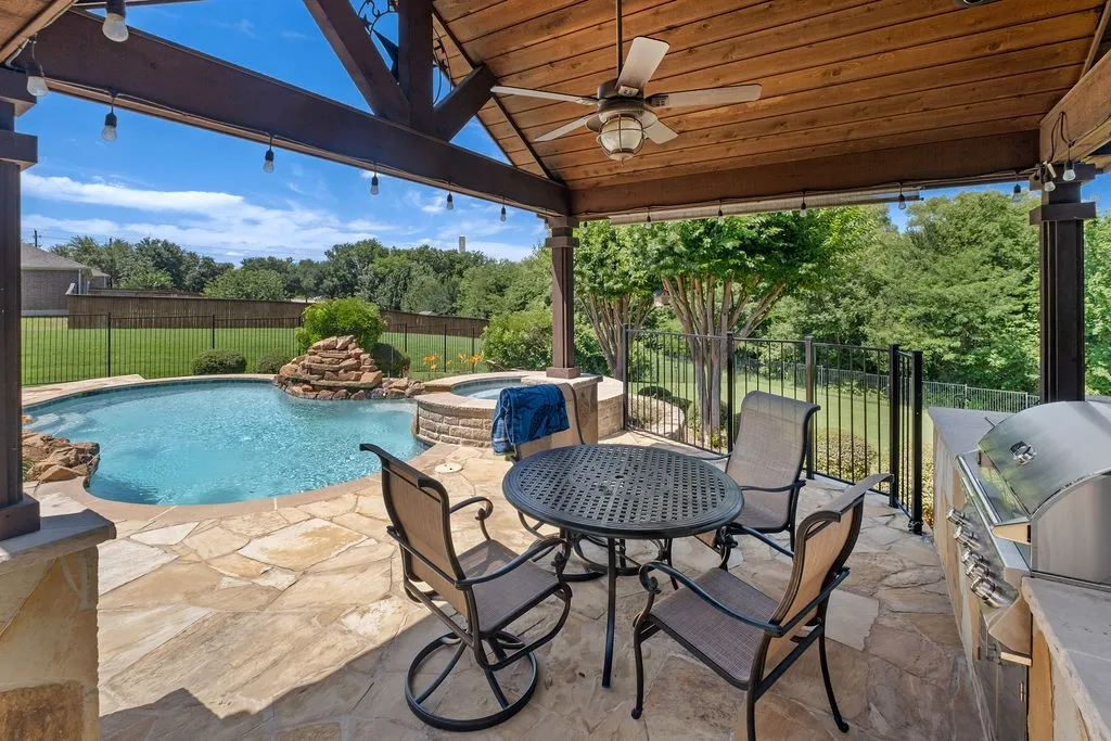 Covered patio with a wood-finish ceiling, built-in outdoor grill, flagstone patio, custom pool with water feature, and integrated spa