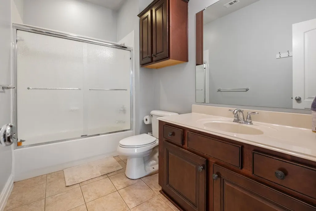 Tub/shower combination with sliding frosted glass doors, a single vanity with wood-finish cabinetry, integrated sink, and an expansive wall-mounted mirror