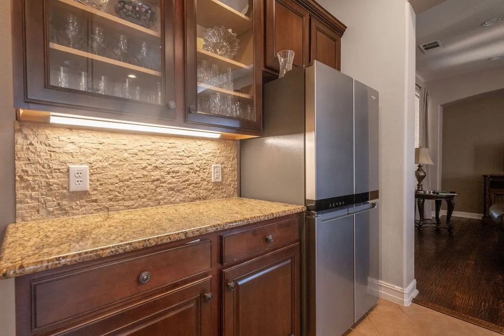 Rich wood-finish cabinetry, stone-finish backsplash, built-in under-cabinet lighting, and a stone-finish countertop