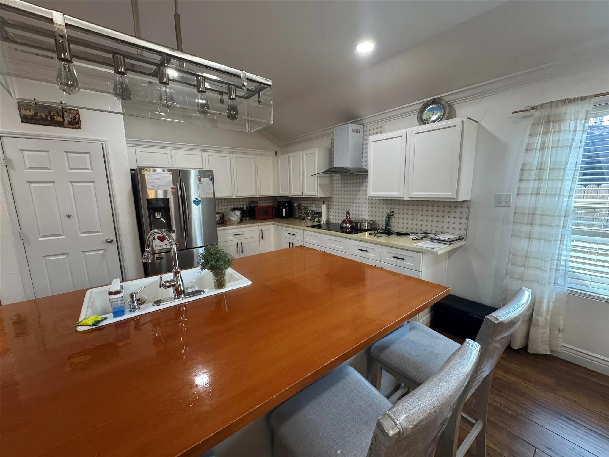 Island kitchen featuring white cabinetry, stainless steel appliances, wood-finish flooring, and an island with an integrated sink