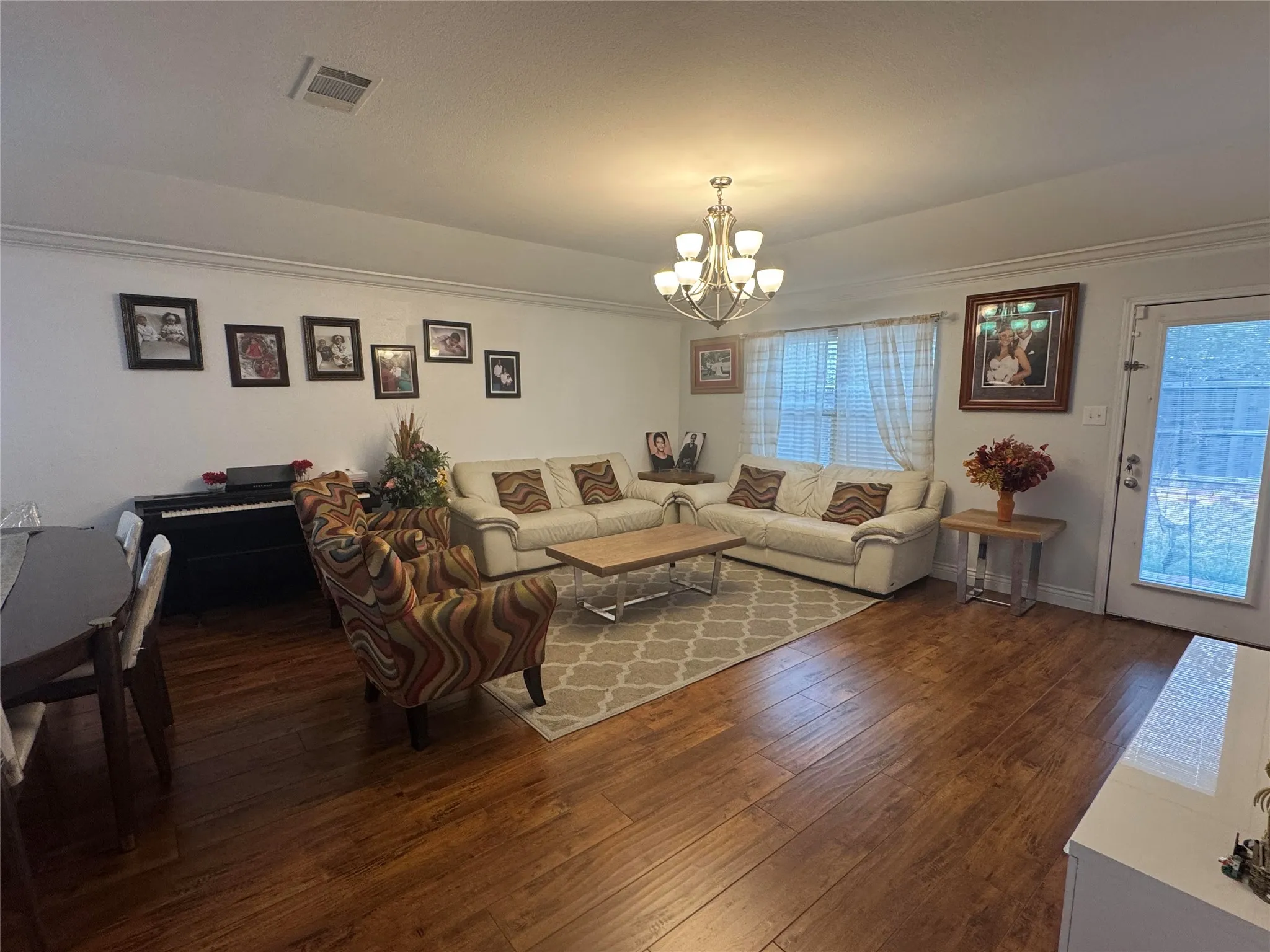 Hardwood flooring throughout, crown molding, white walls, and a multi-arm chandelier