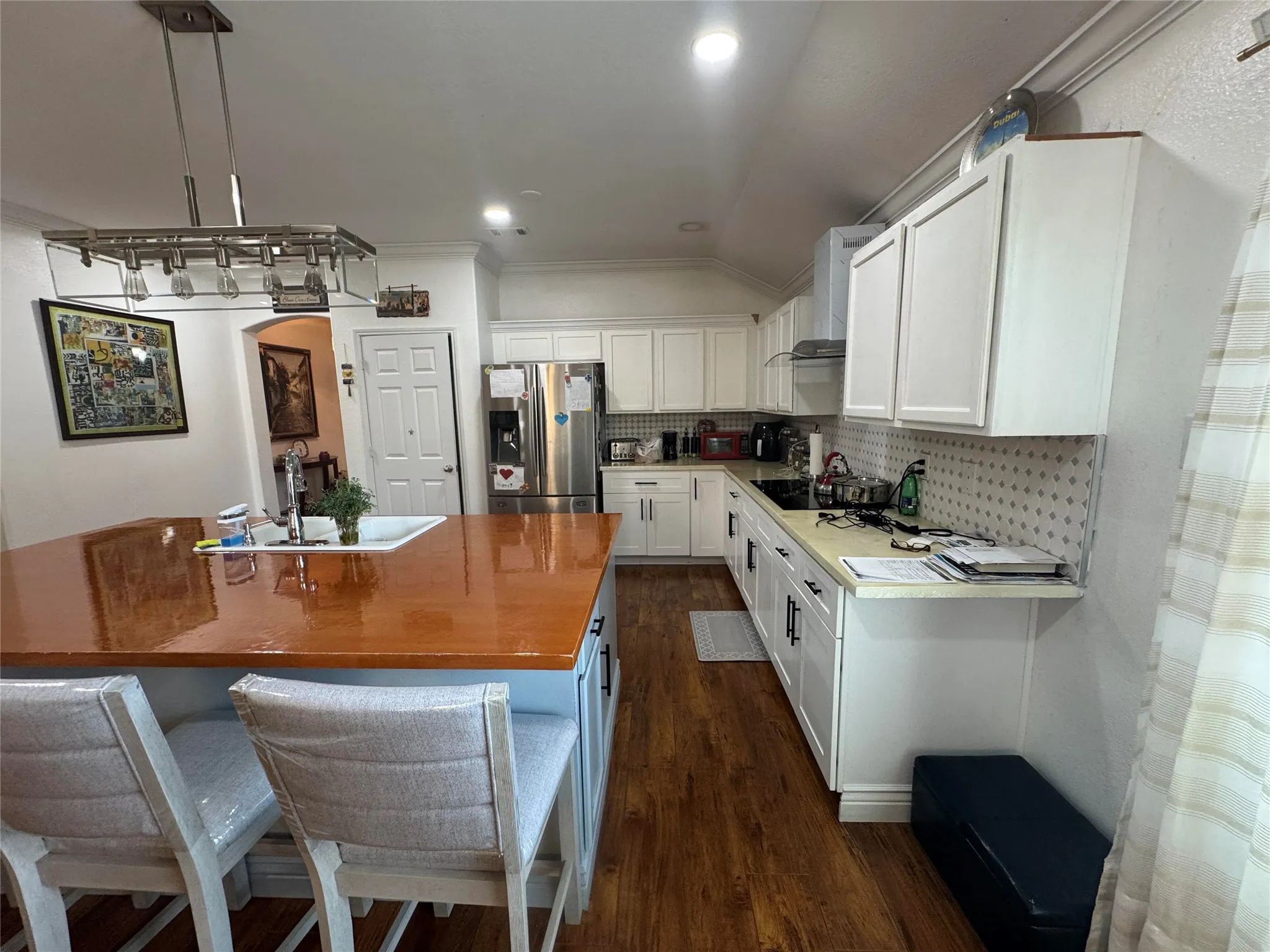 Kitchen featuring a large island with an integrated sink, wood-finish flooring, white cabinetry, recessed lighting, and a stainless steel refrigerator