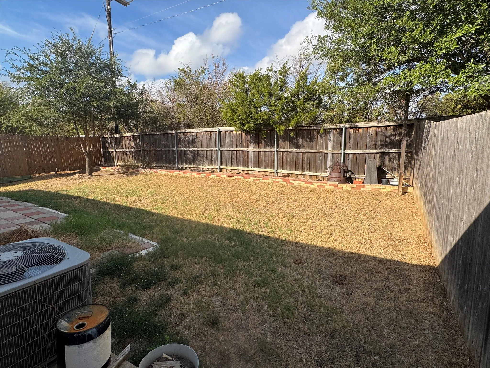 Expansive backyard featuring wood privacy fencing, mature trees, and a ground-level patio with stone pavers