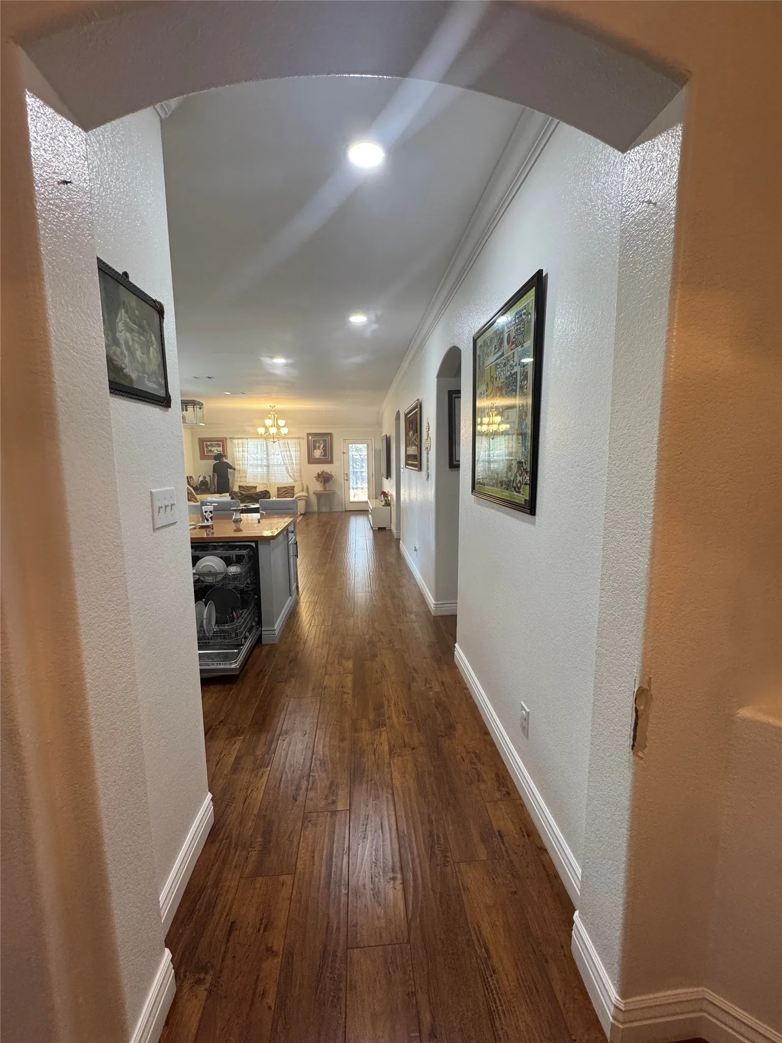 Arched doorway opening to a hallway with wood-finish flooring, recessed lighting, and crown molding